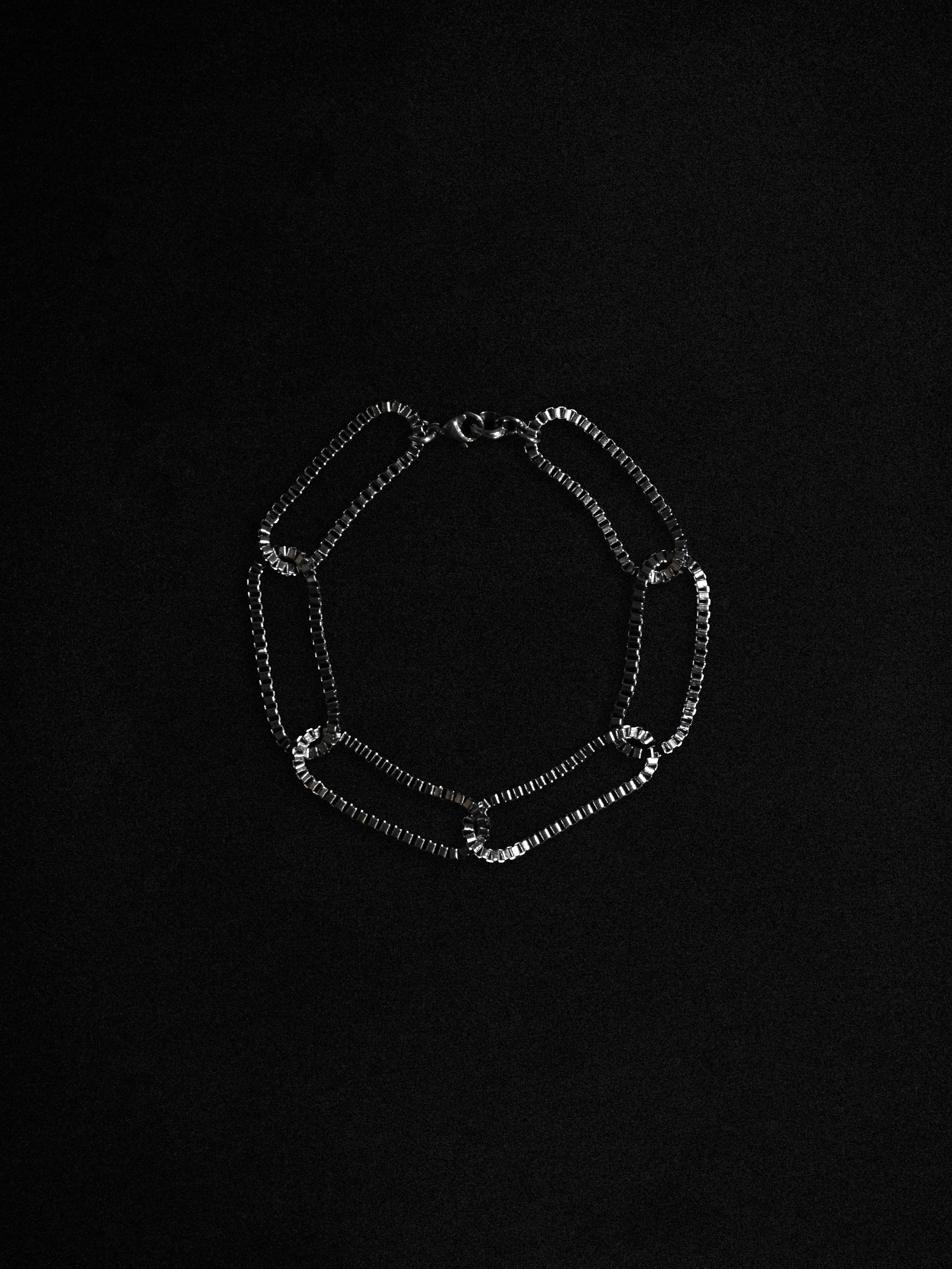 A silver bracelet with slender box chains, displayed against a black background.