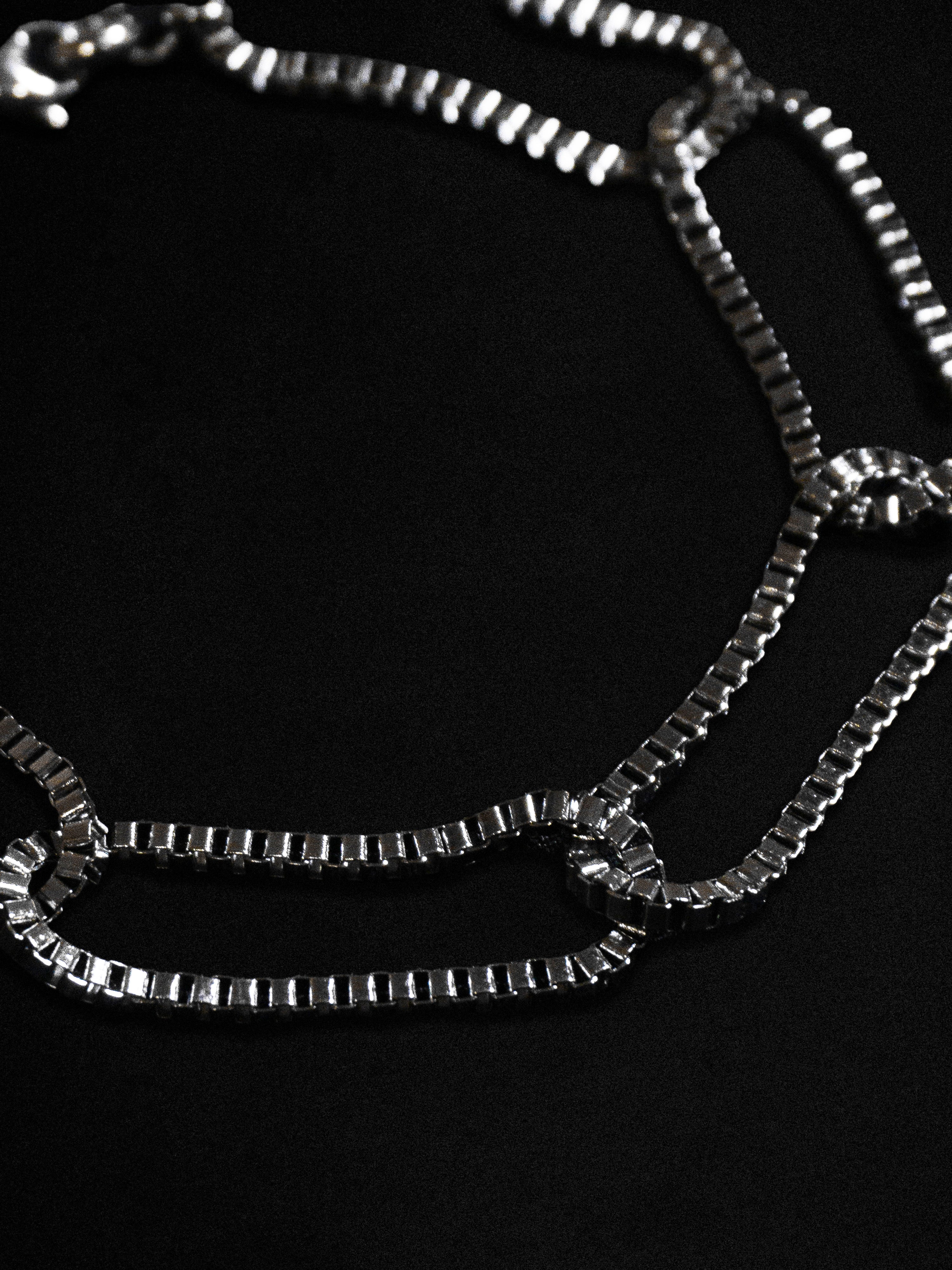 Close up of a slender loop box chain bracelet on a black background 