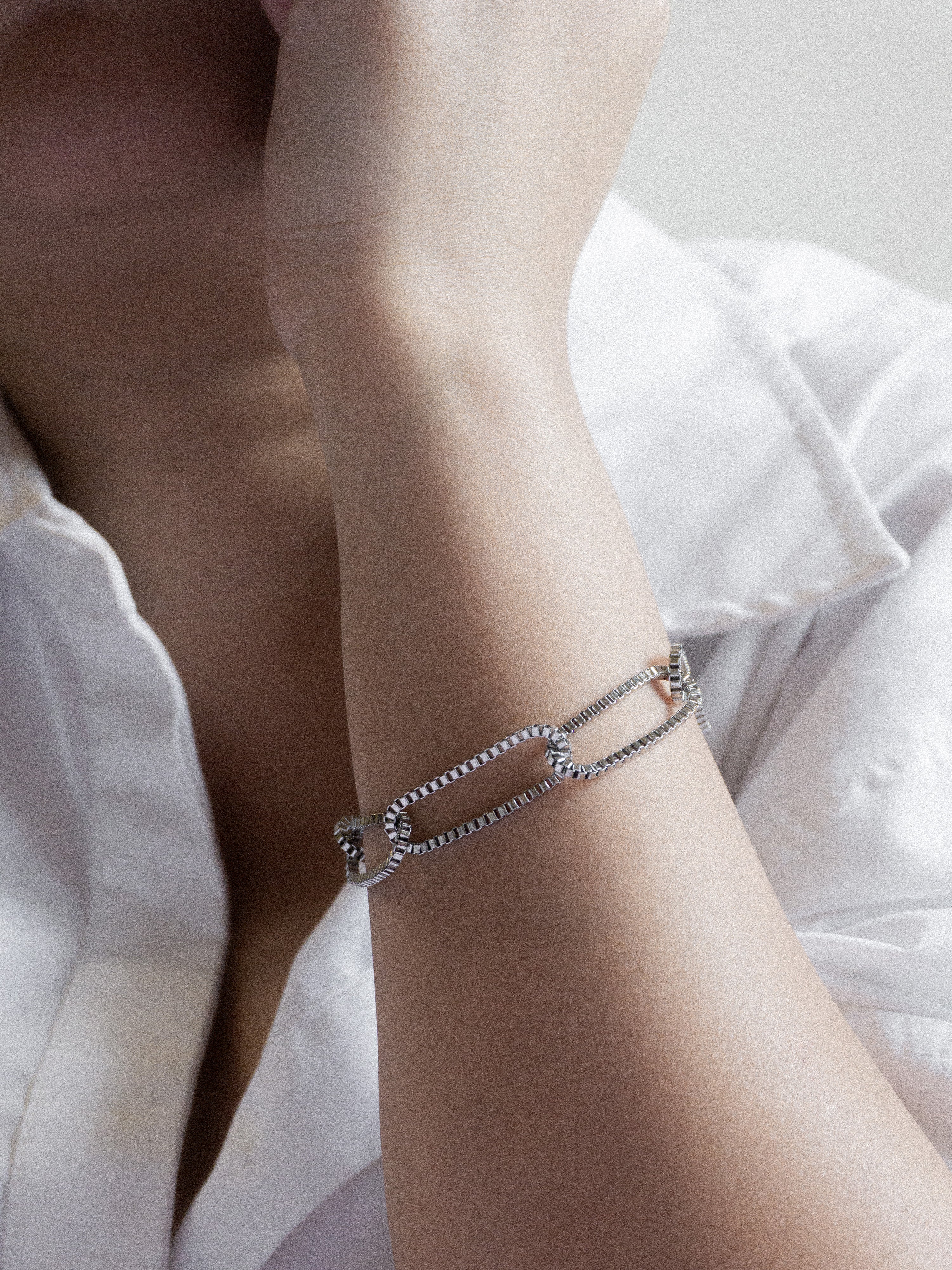 Close-up of a wrist wearing a silver bracelet with a blurred white shirt background