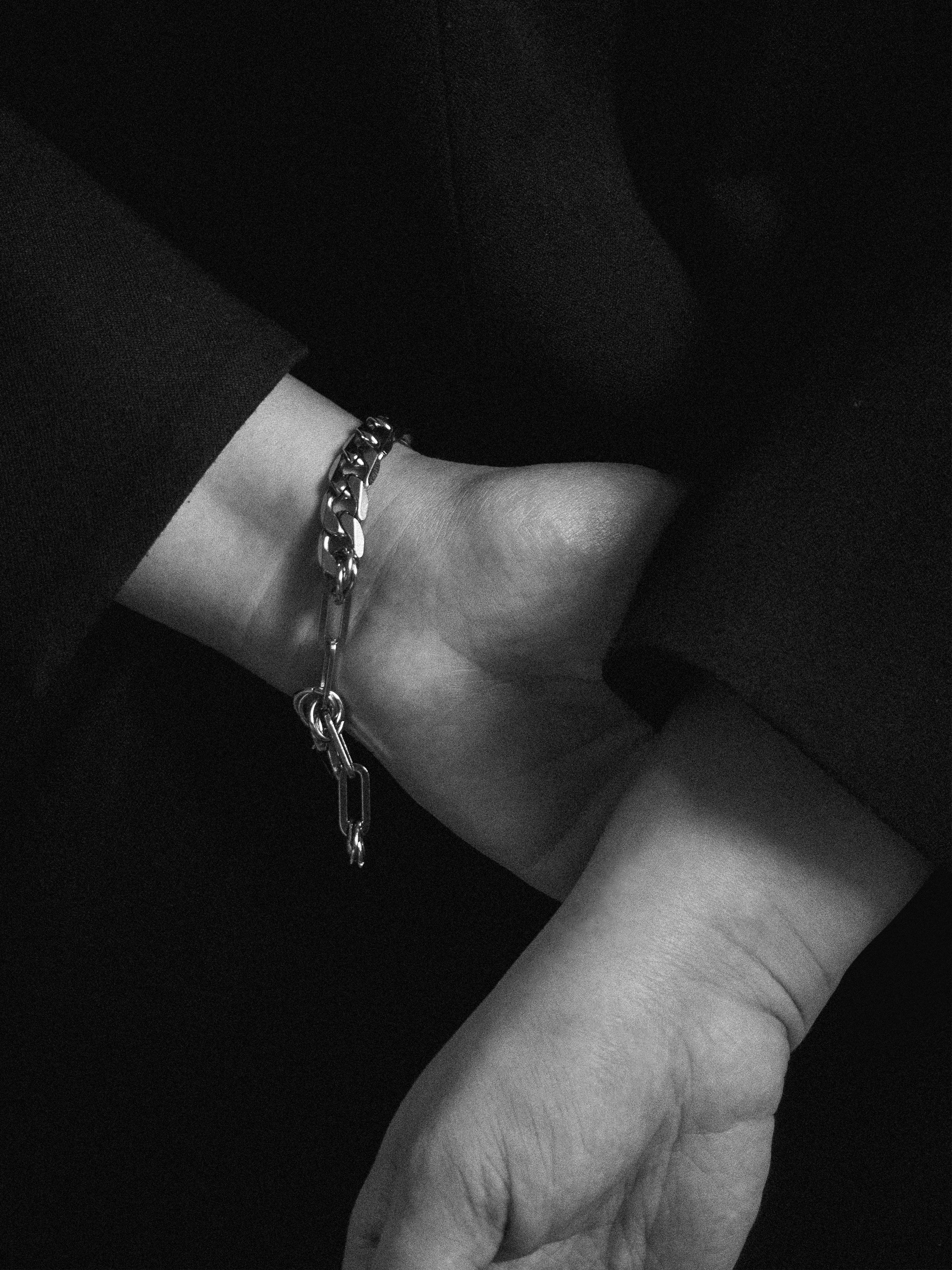 Close-up of a wrist wearing a chain bracelet with a dark background