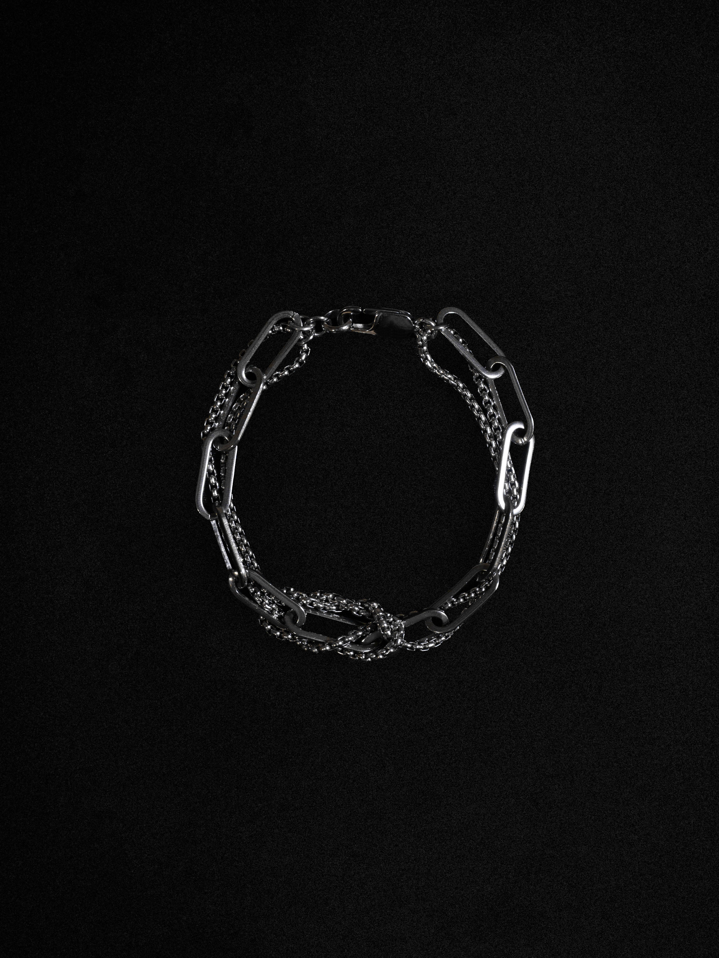 A silver bracelet with layered knots and a bold clasp, displayed against a black background.