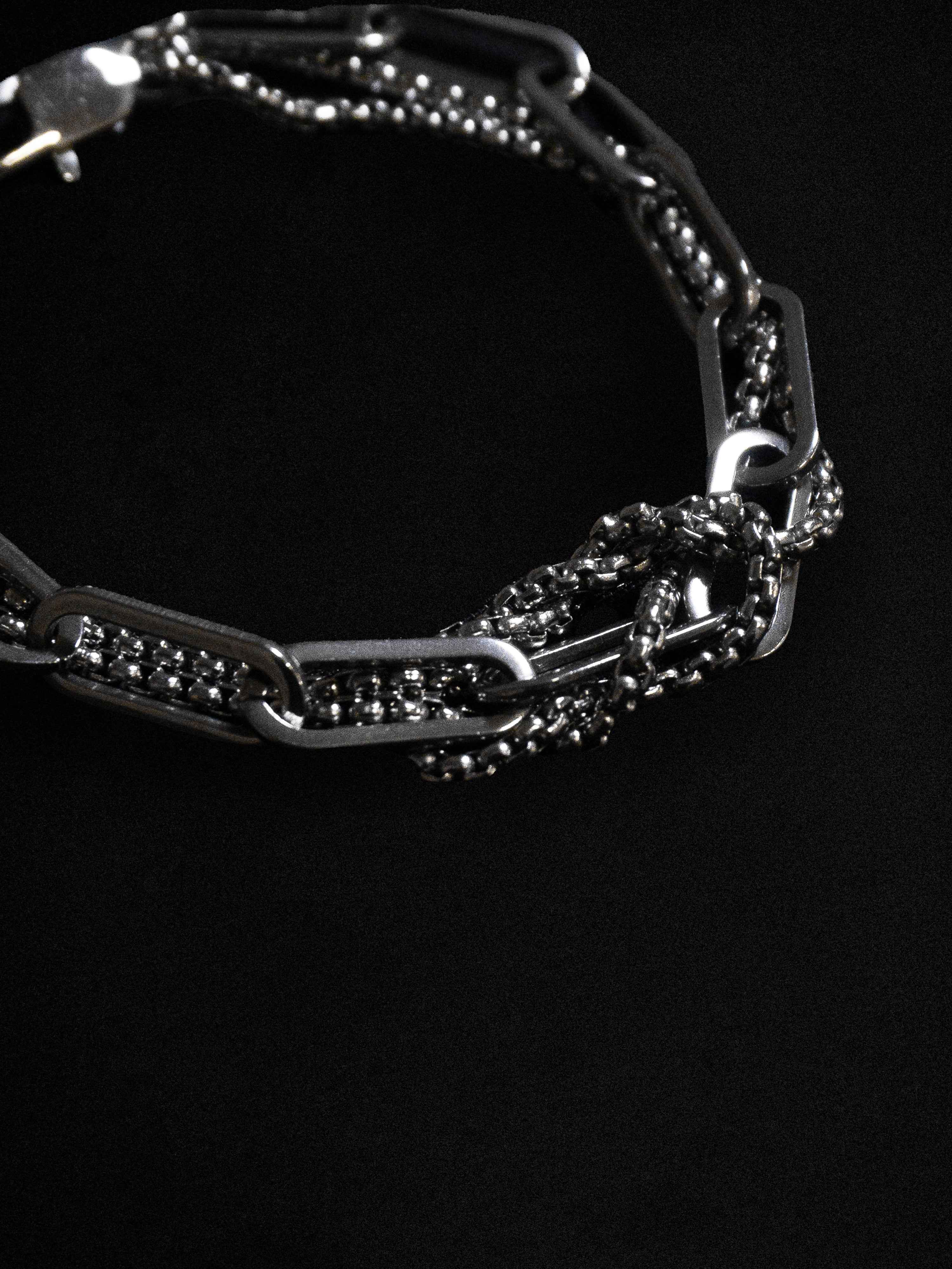 A close up of a knotted chain bracelet against a black background 