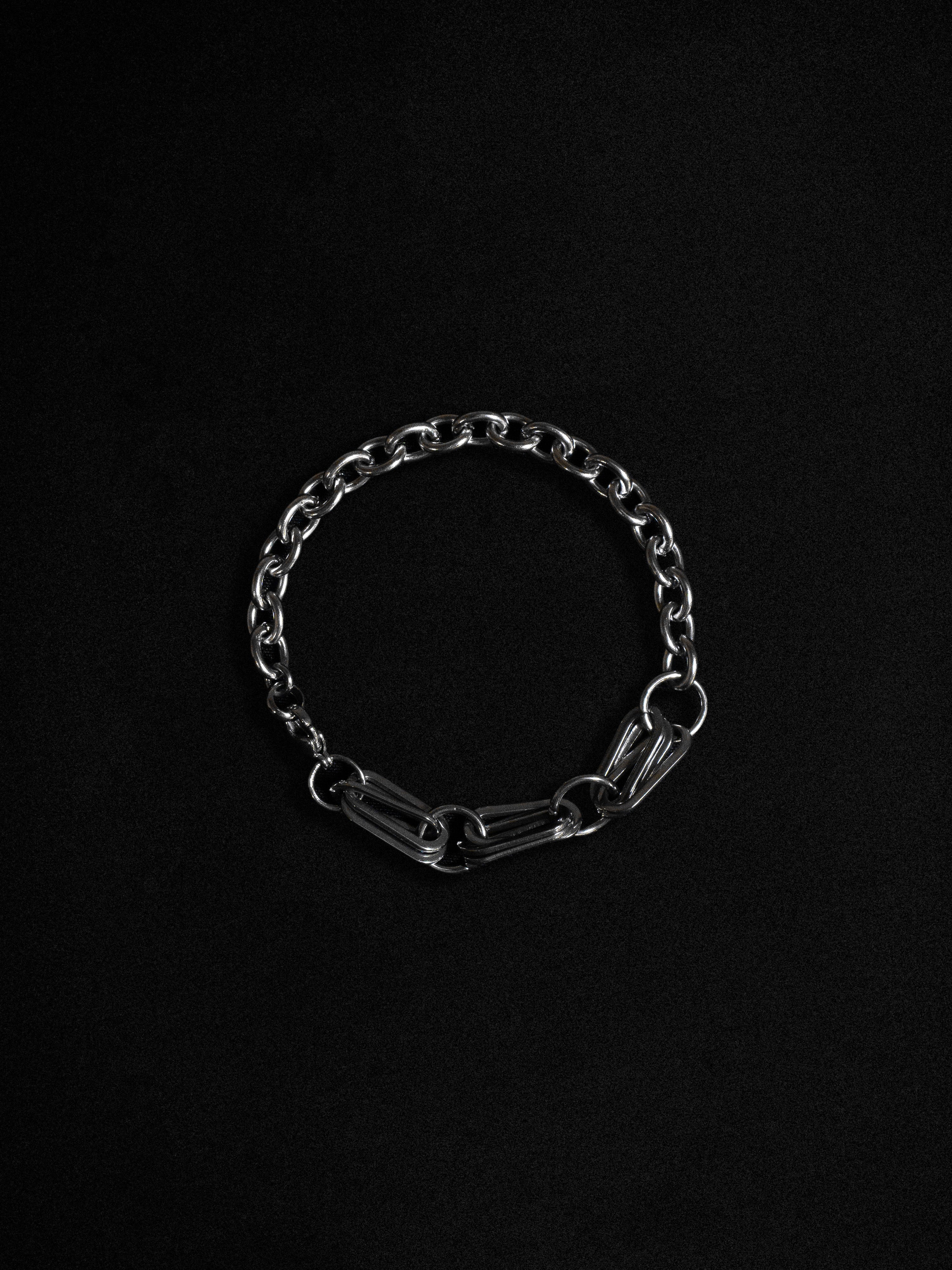 A silver bracelet with a chain and paperclip design, displayed against a black background.