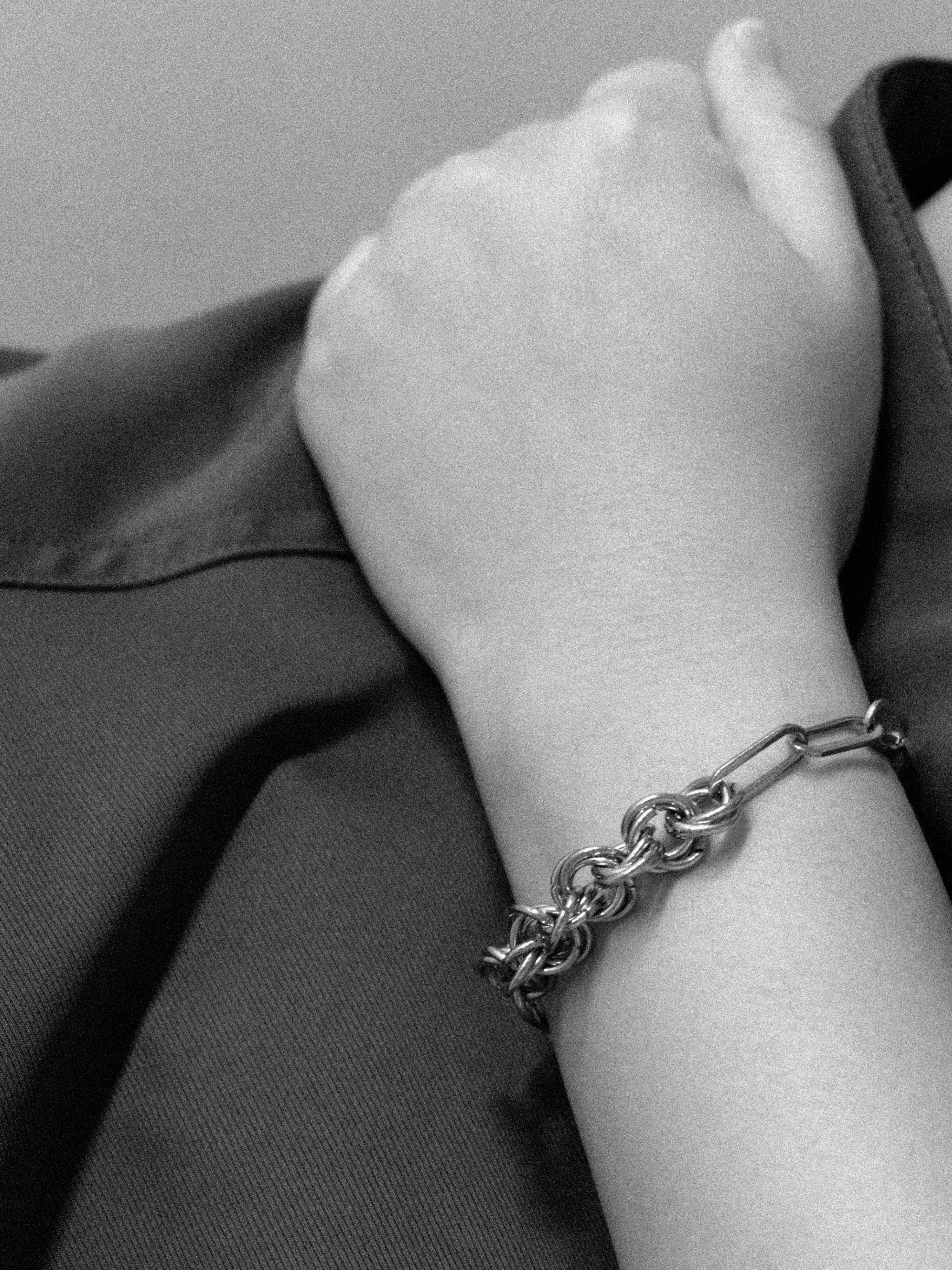 Close-up of a hand wearing a chain bracelet on a neutral background