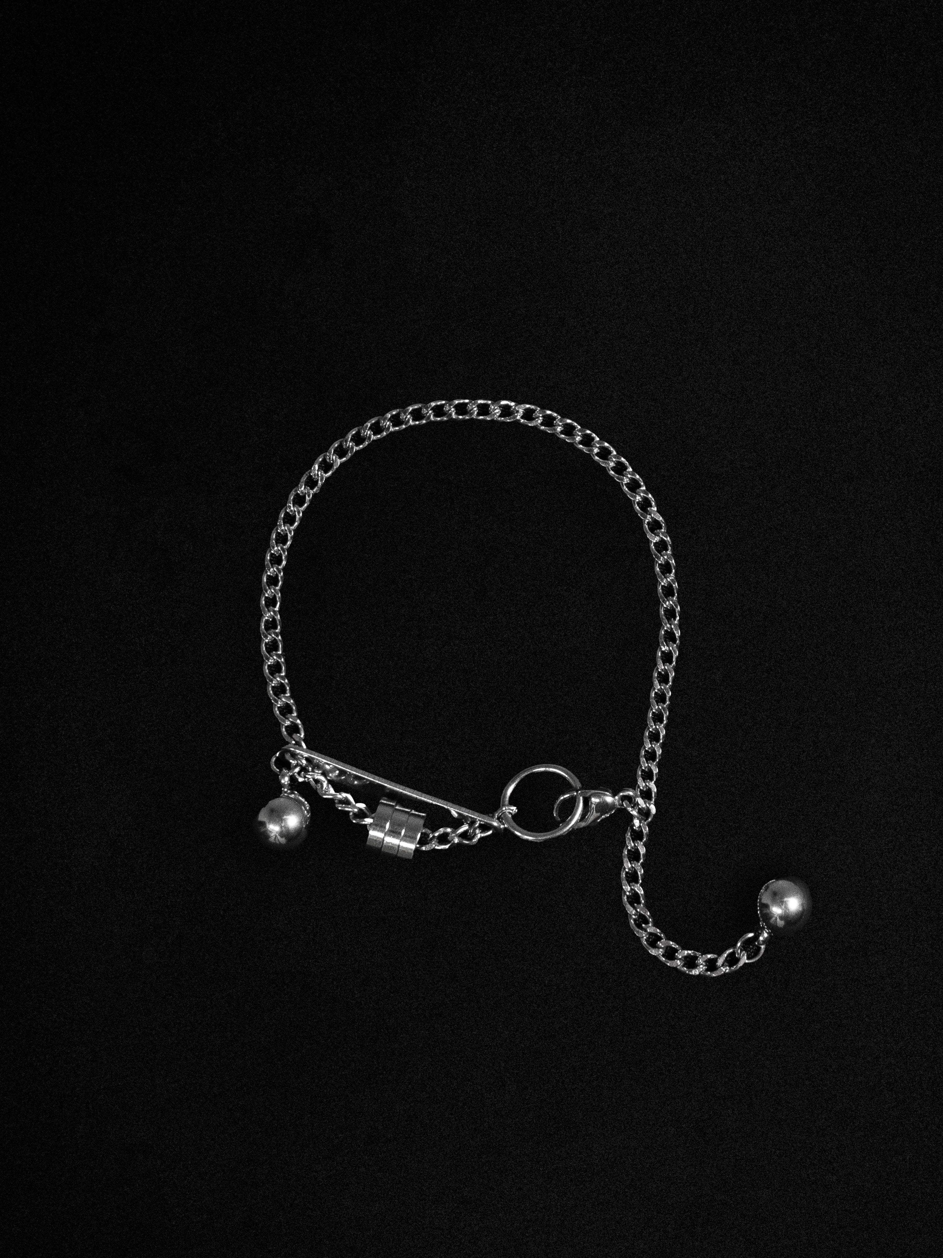 A silver-toned bracelet with an asymmetrical design and a spherical drop, displayed against a black background.