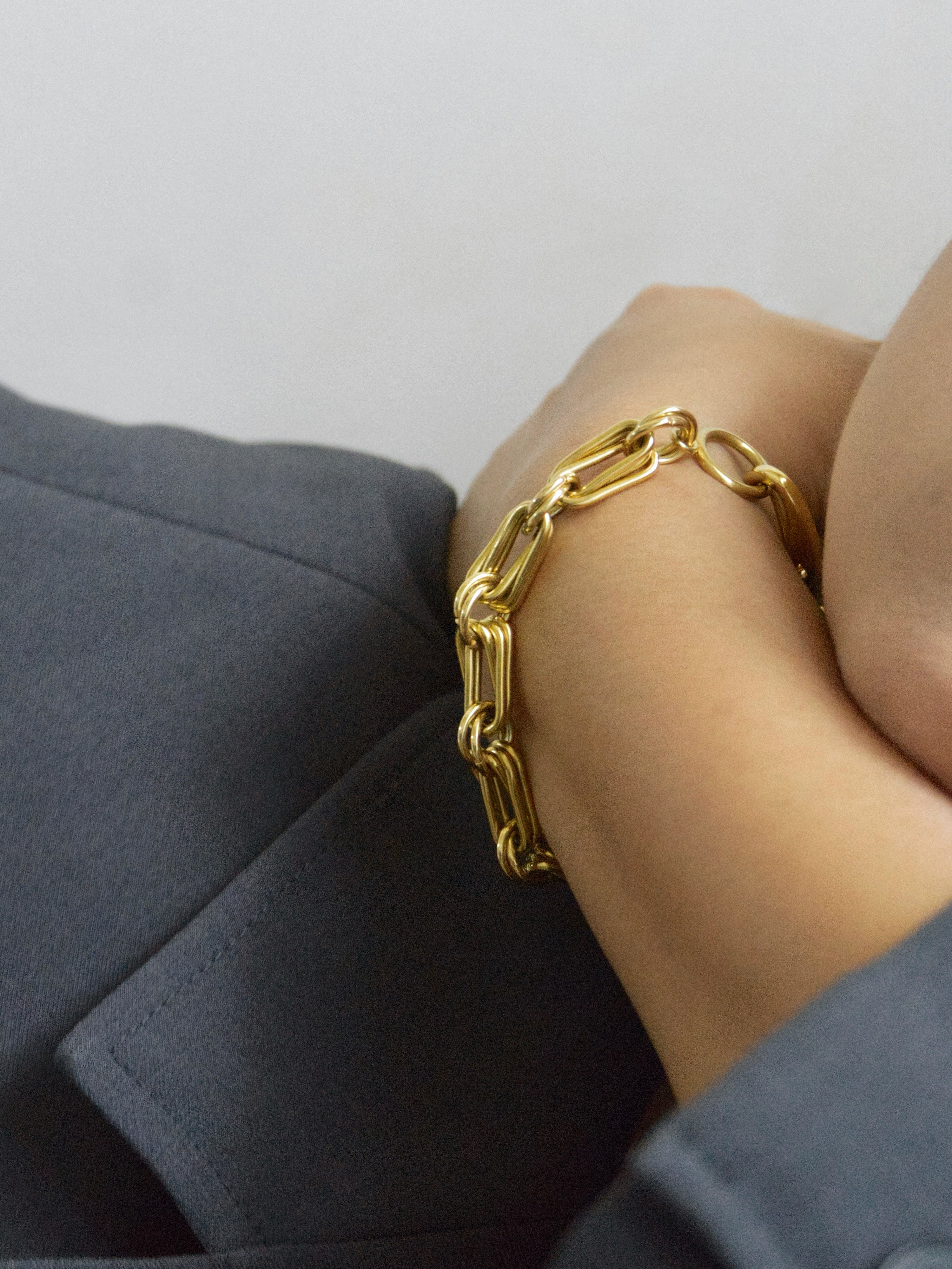 A close-up of a person wearing a chunky gold chain link bracelet on their wrist, with a grey blazer sleeve visible.