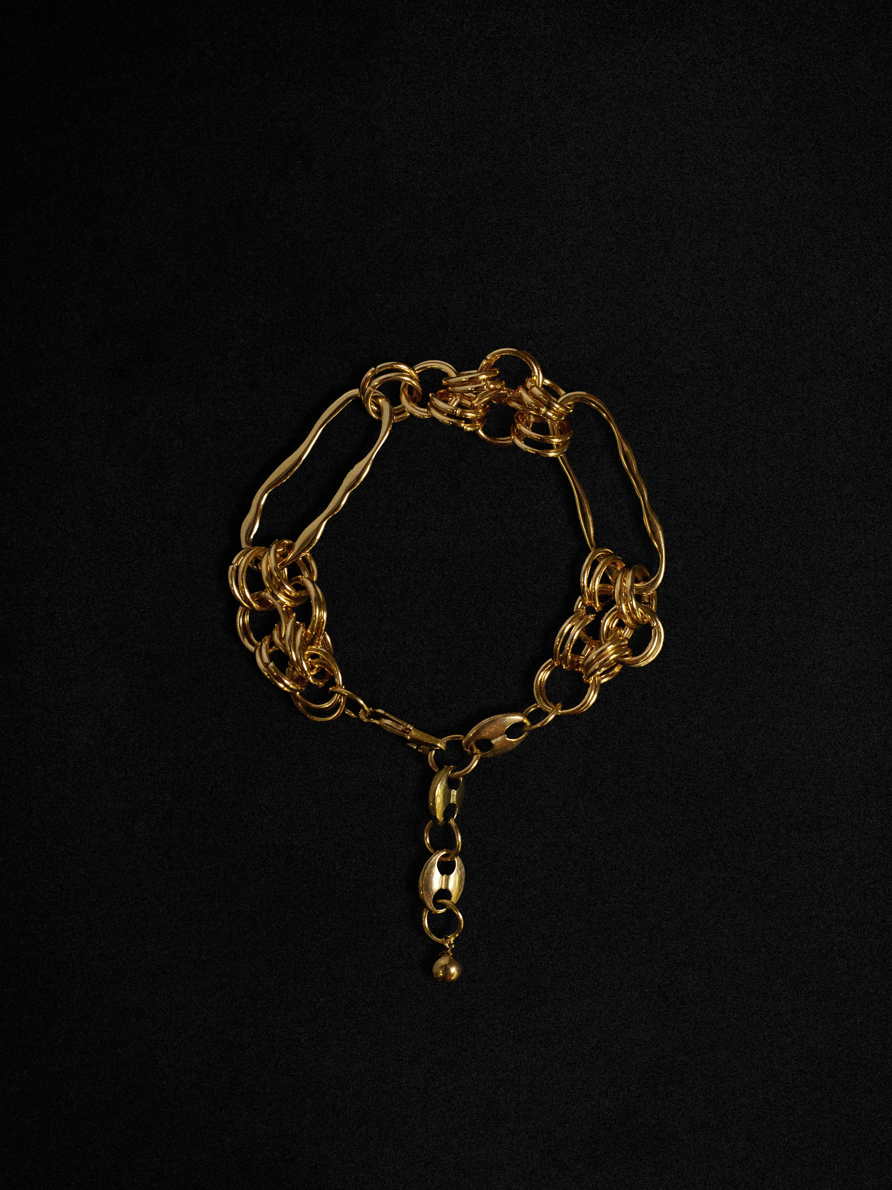 A gold-toned bracelet with a textured, wave-like design, displayed against a black background.