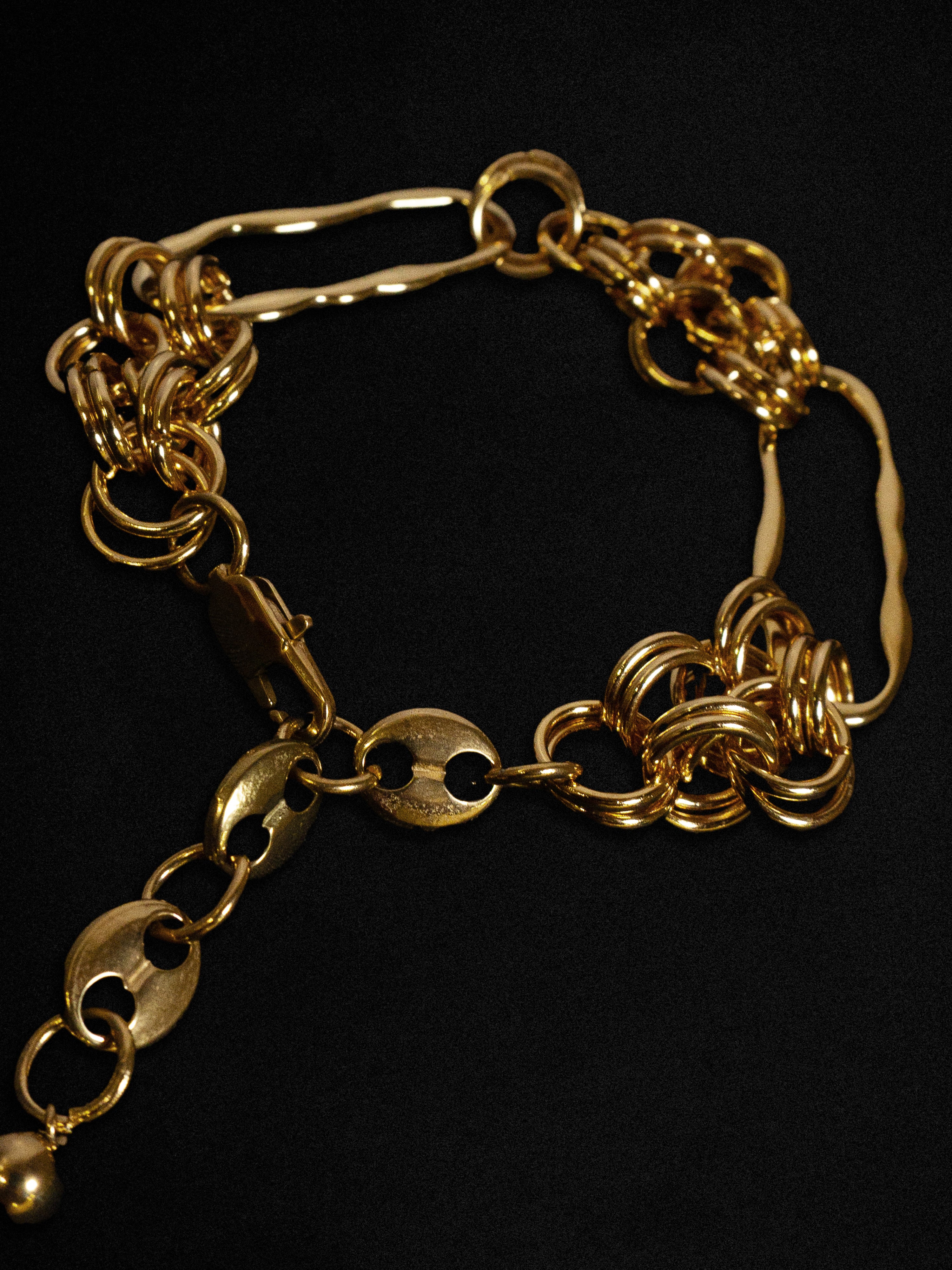 Close up of a gold bracelet with wave-like hardware details on a black background 