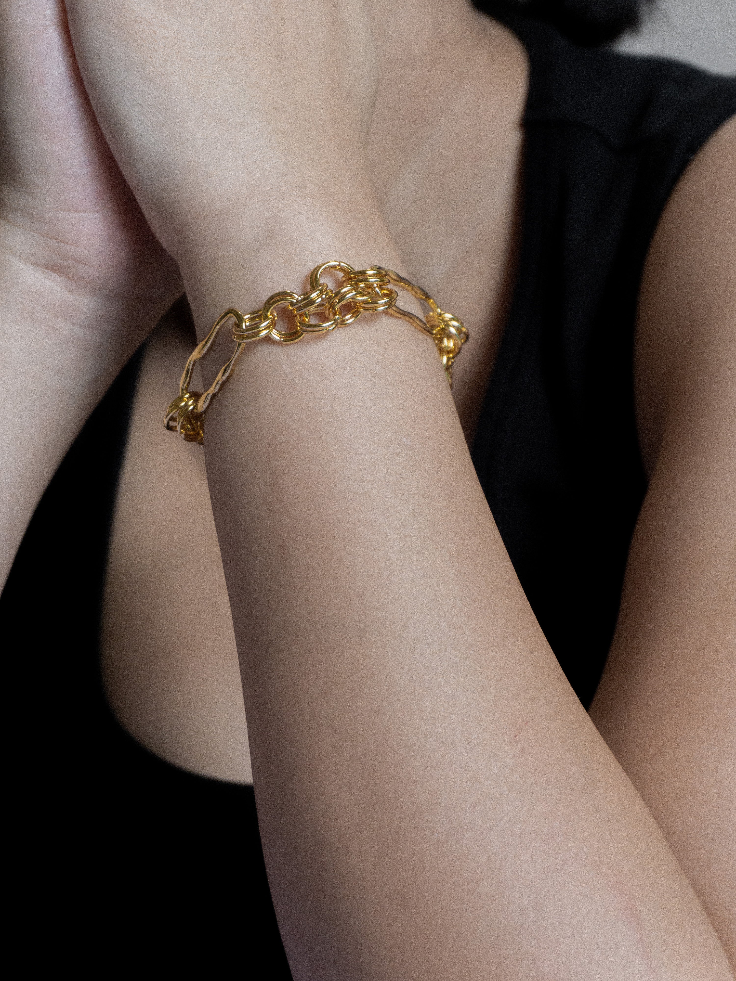 Gold chain bracelet on a wrist against a dark background