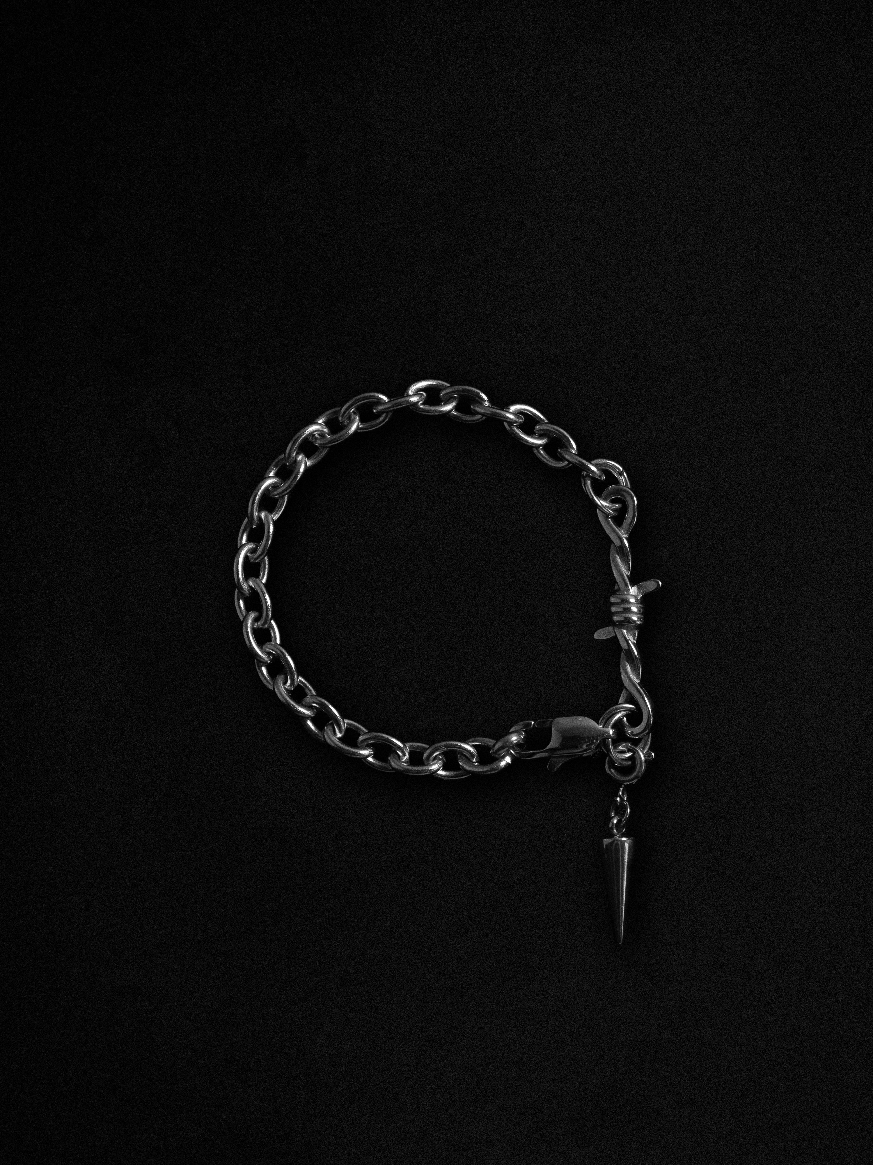 Silver chain bracelet with a pine cone charm on a black background