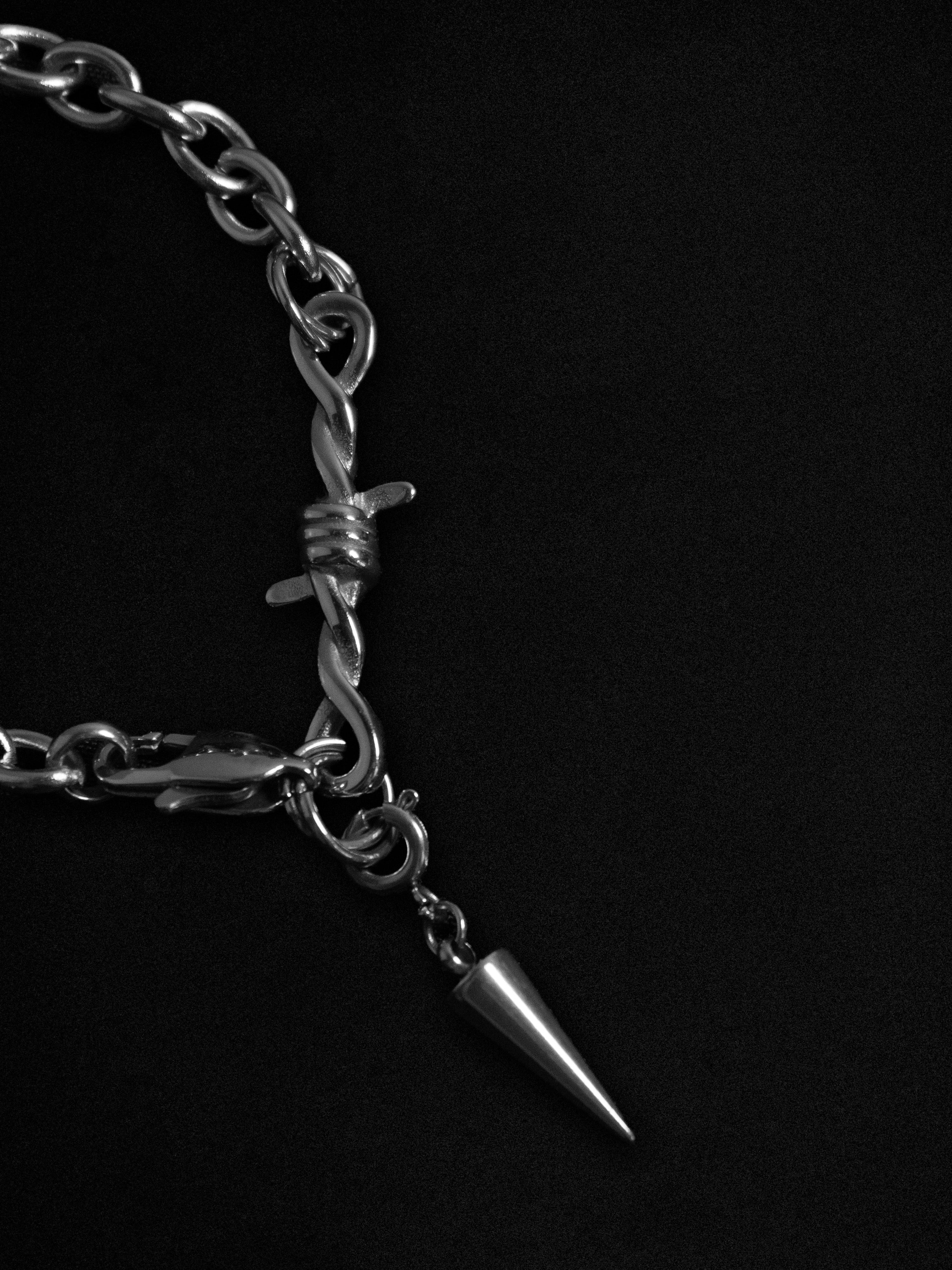 Silver bracelet with barbed wire and pine cone charm on a black background