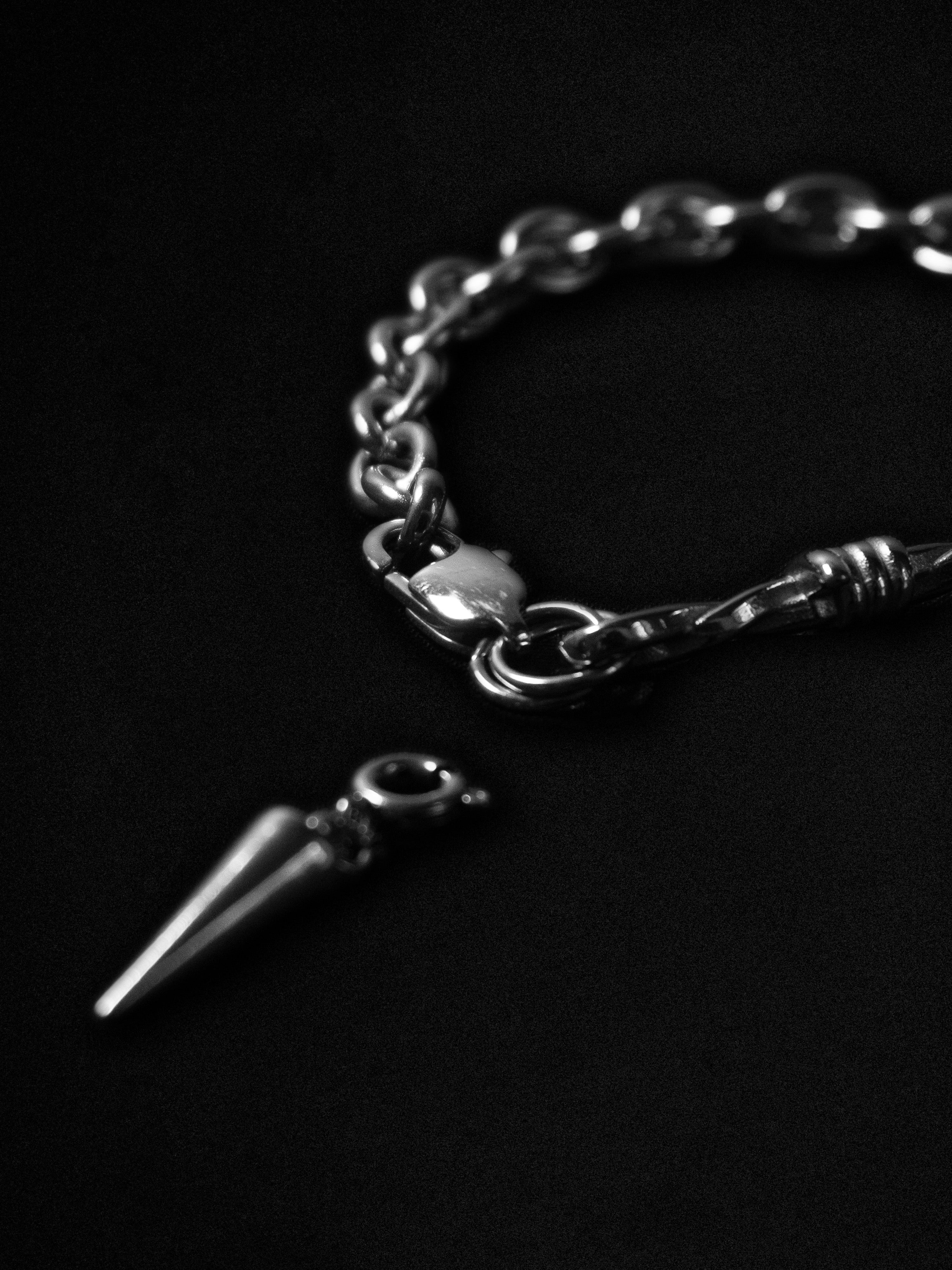 Silver chain bracelet with a spike-like charm on a black background
