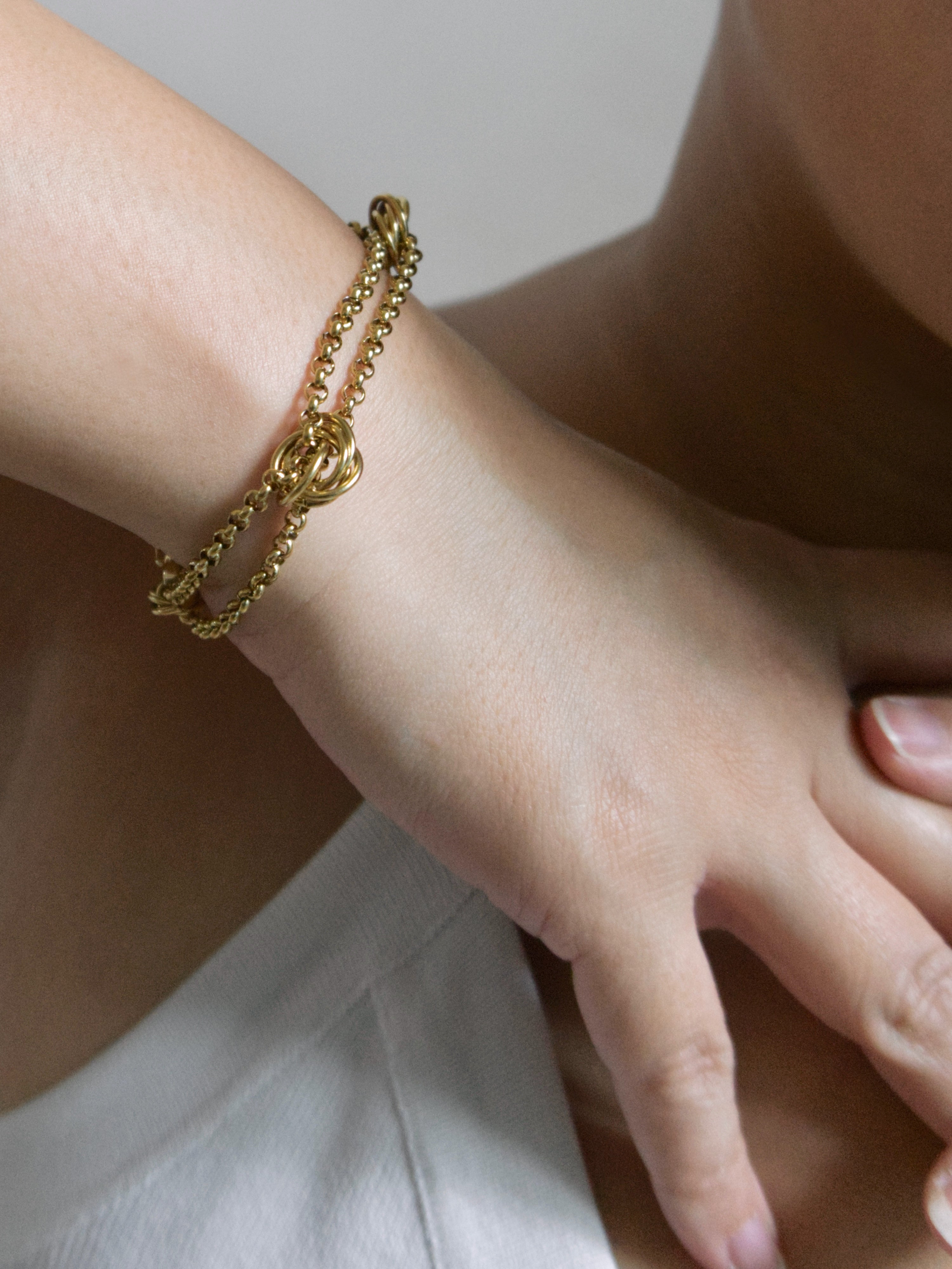 A close-up of a person's wrist wearing a delicate gold chain bracelet with a central interlocking double-ring motif.