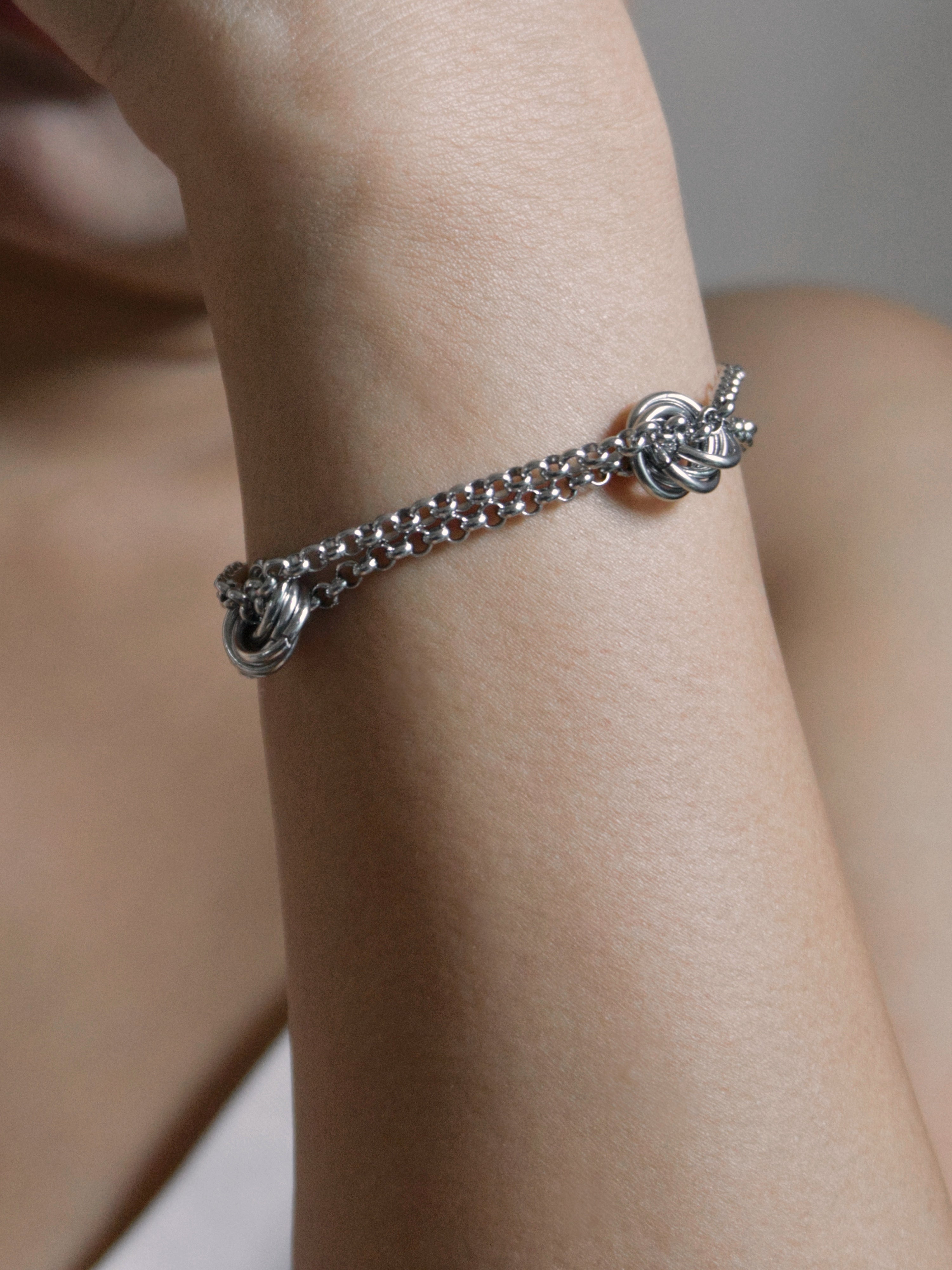A silver chain bracelet with knotted decorative ends, shown worn on a person's wrist.