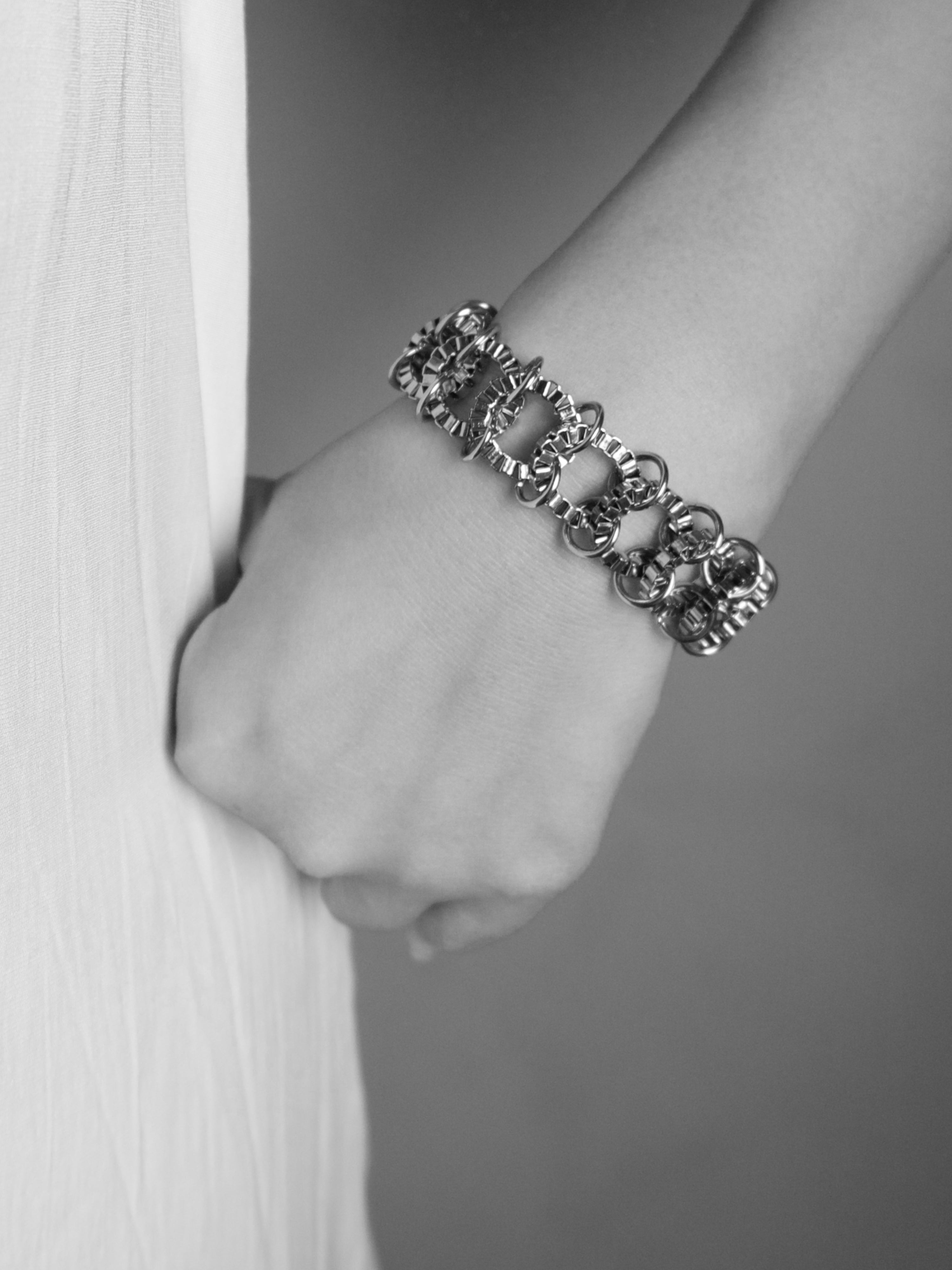 A close-up of a person's wrist wearing a textured, multi-strand silver chain bracelet, shown in a black and white photograph.