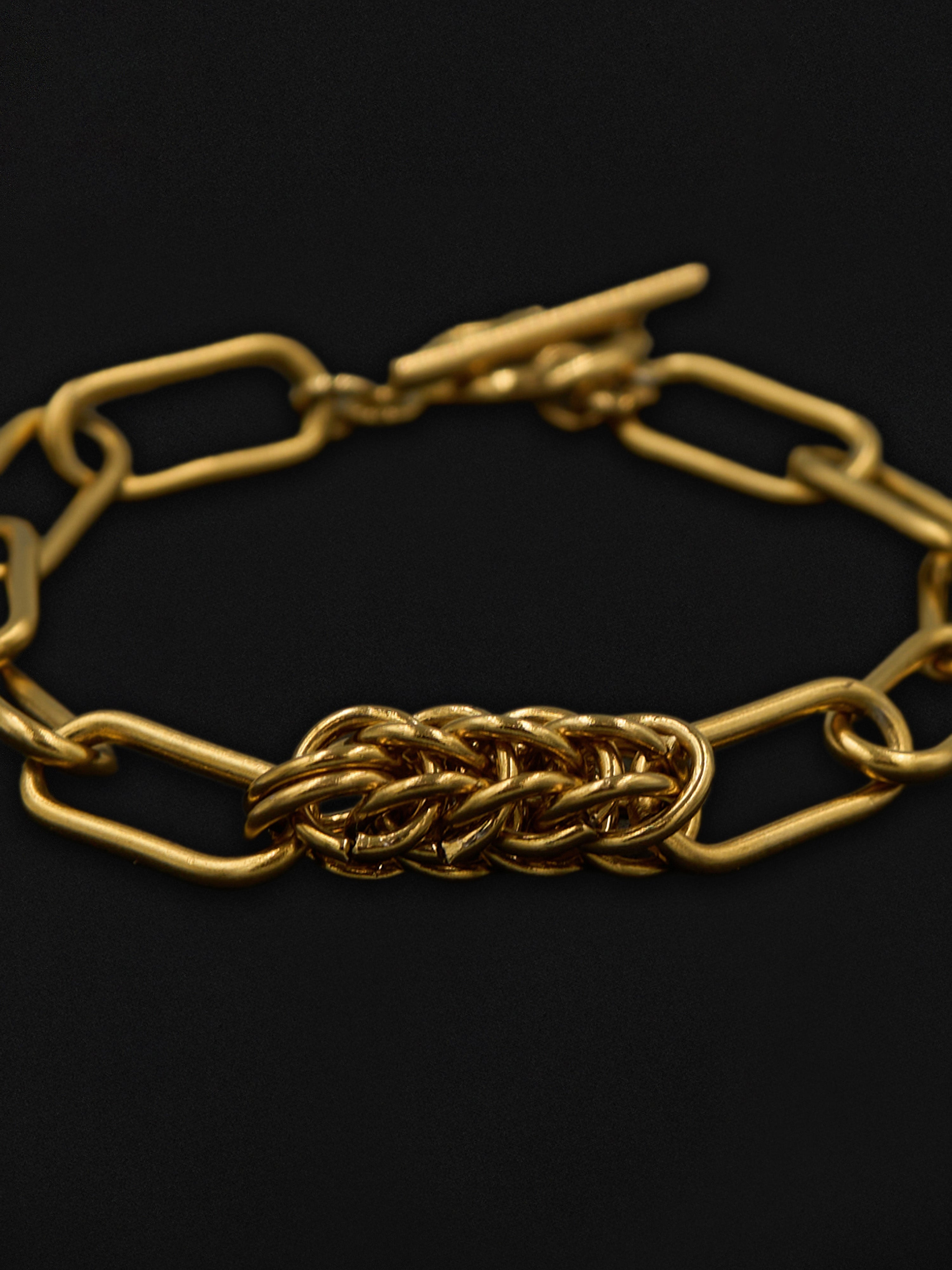 Gold chain bracelet with a chainmaille pendant design on a black background