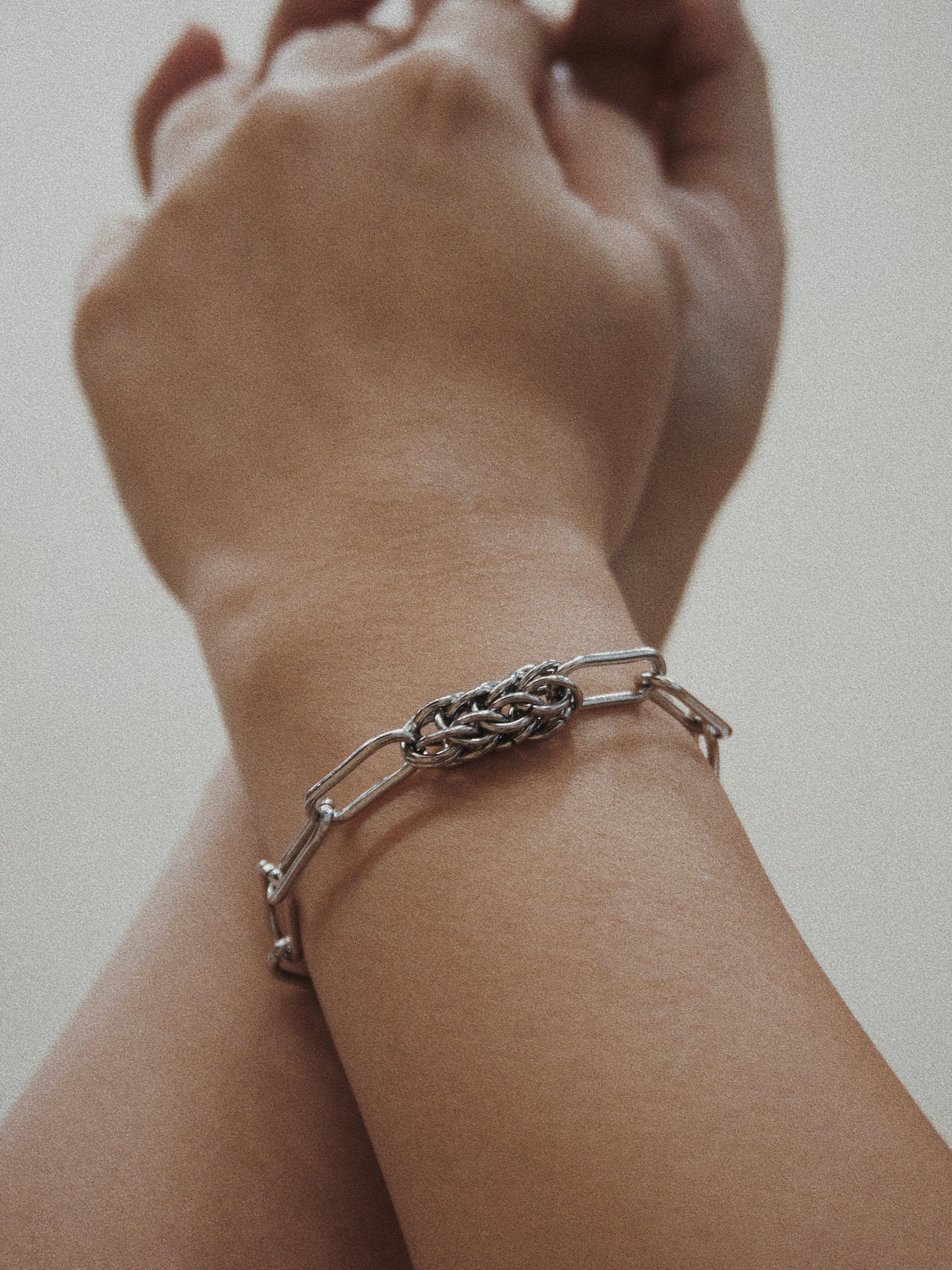 Silver bracelet on a wrist against a neutral background