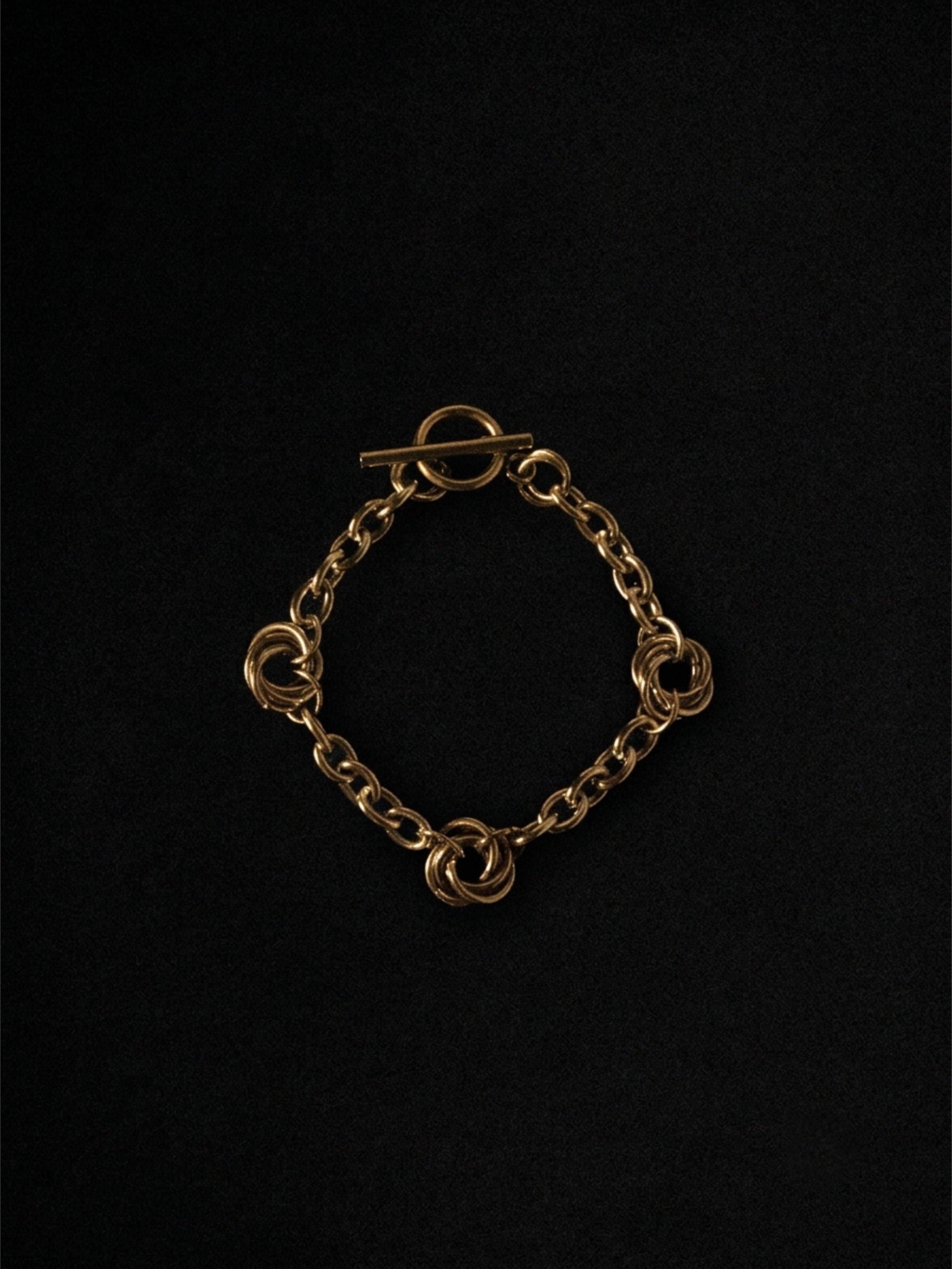 A gold-toned chain bracelet with four interlocking circular links and a toggle clasp, displayed on a solid black background.