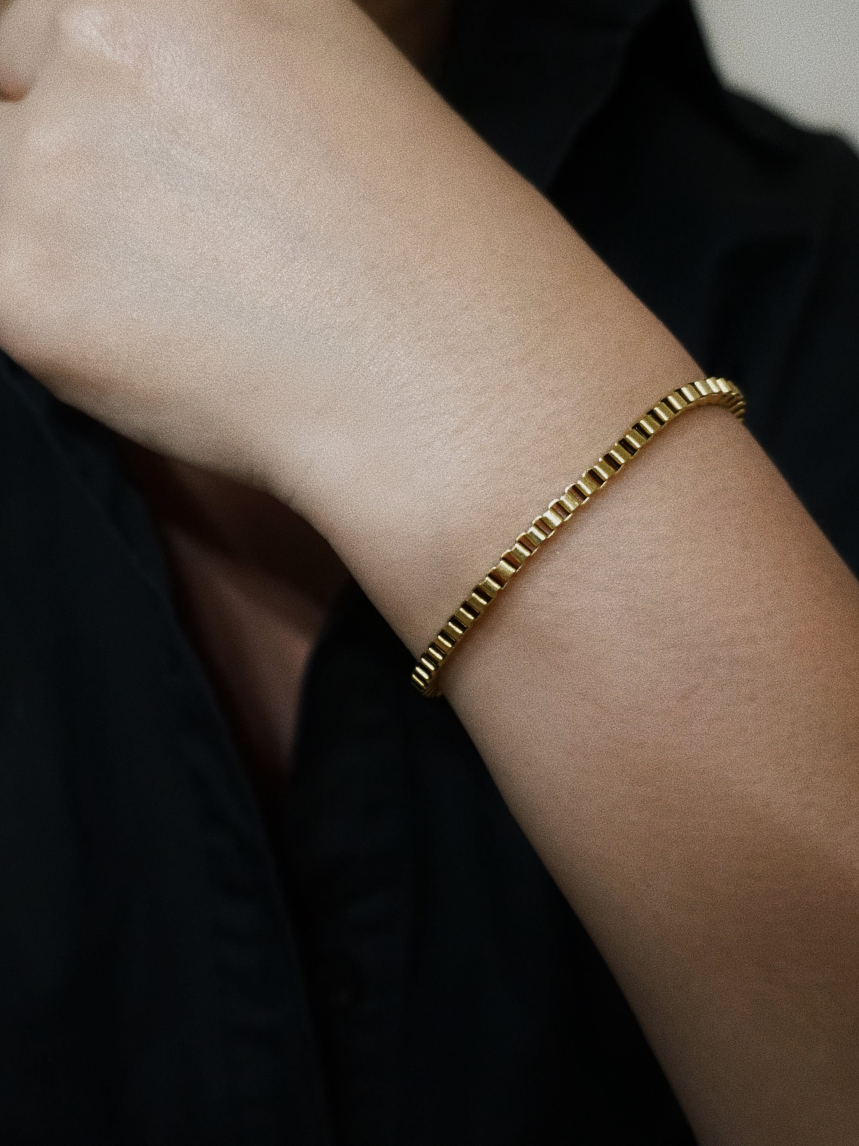 Gold bracelet on a person's wrist against a dark background