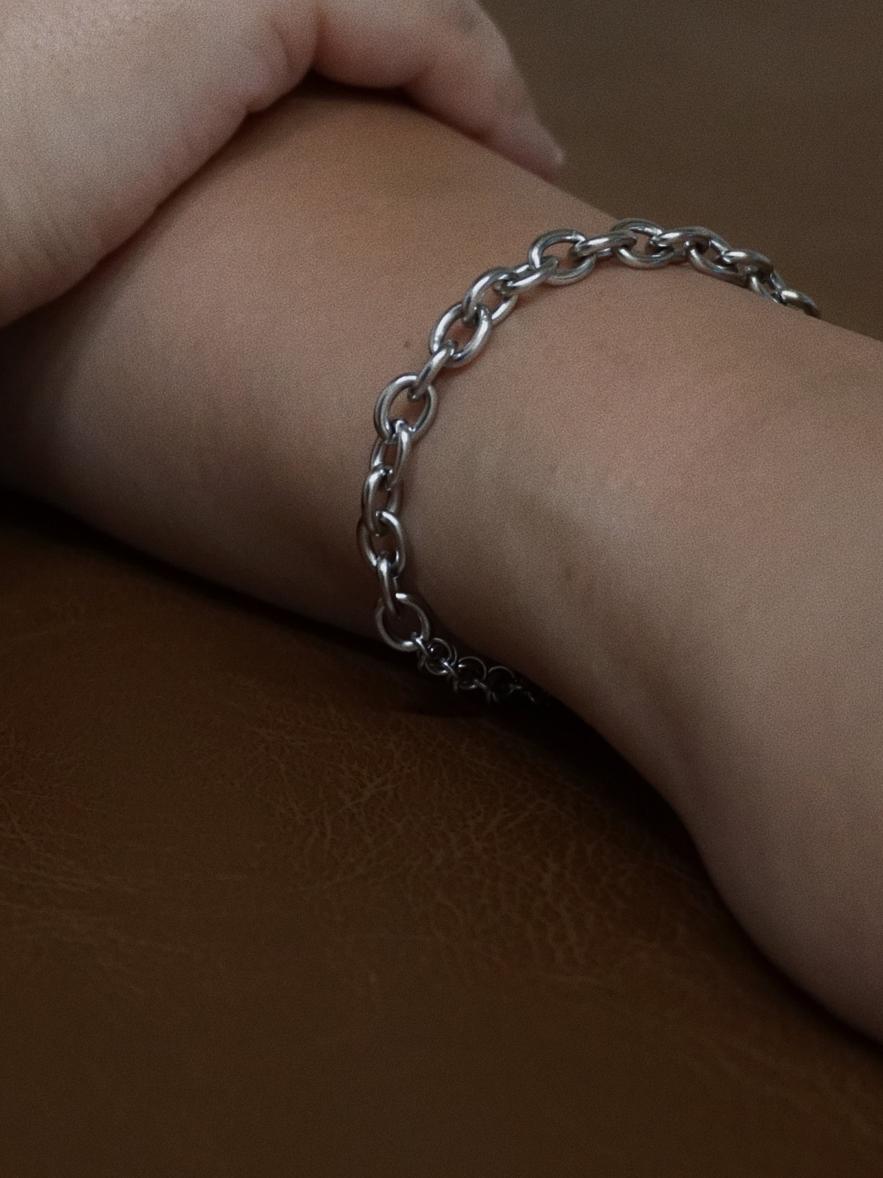 Silver chain bracelet on a wrist against a brown background