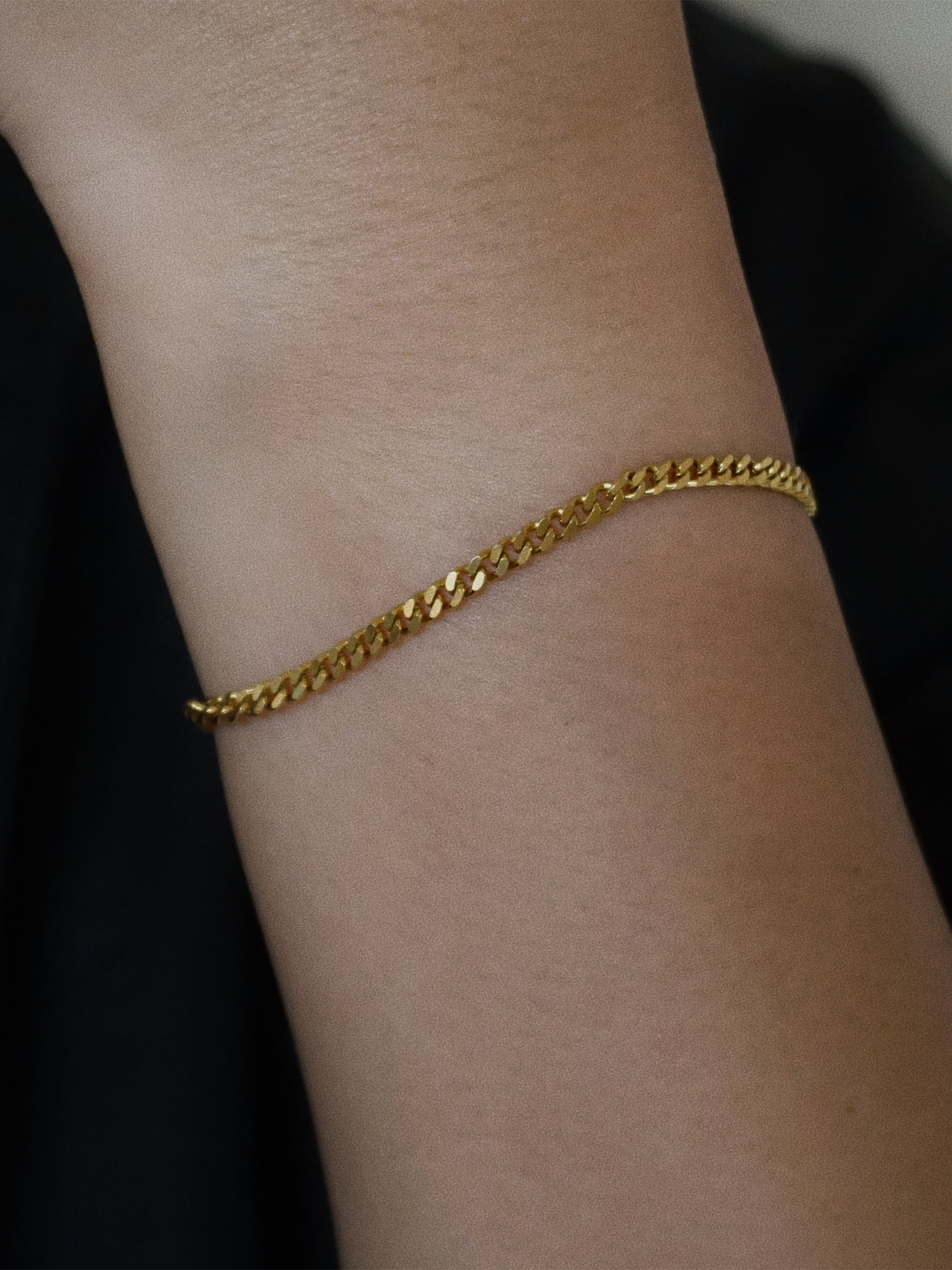 Gold chain bracelet on a wrist against a dark background