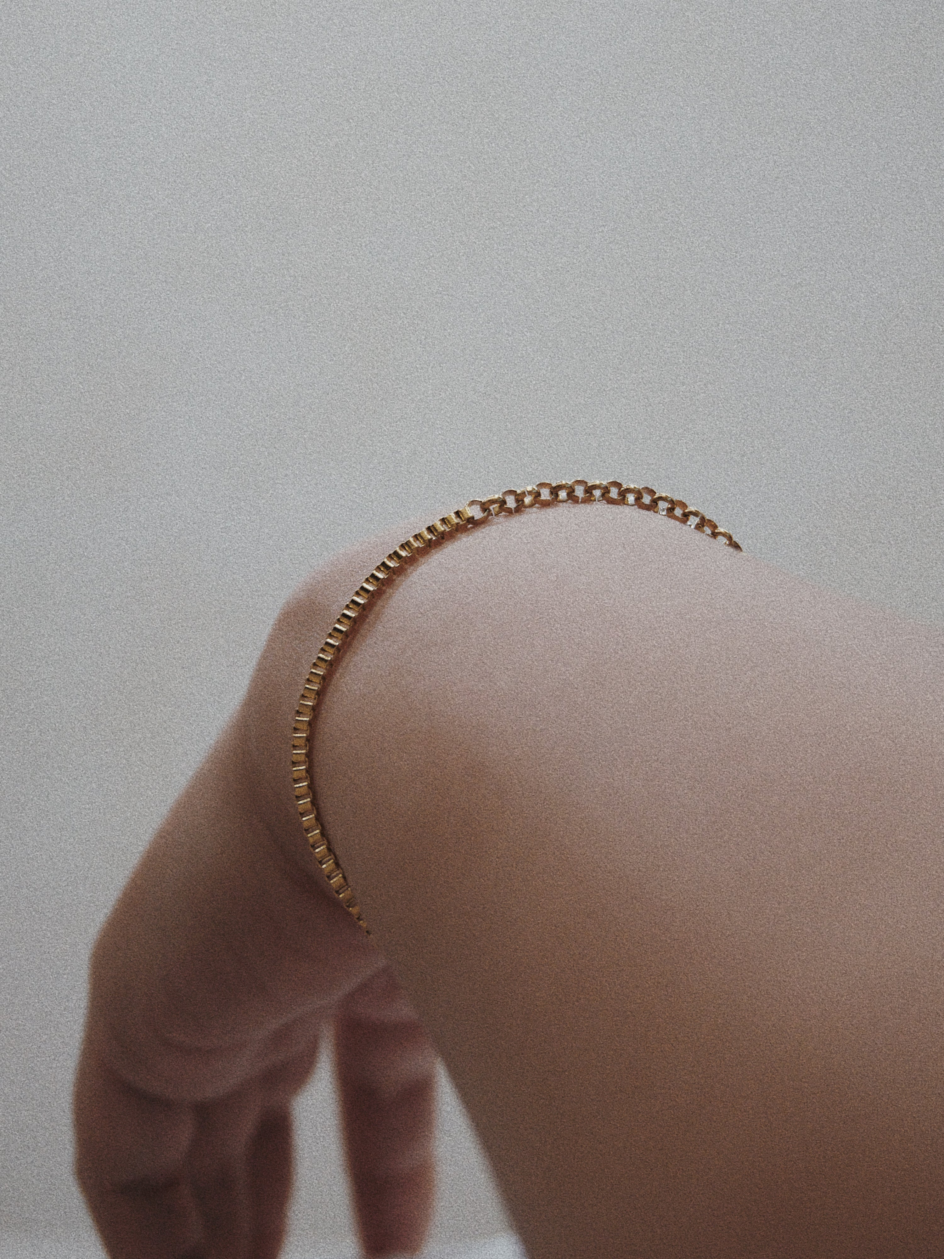 Gold chain bracelet on a wrist against a neutral background