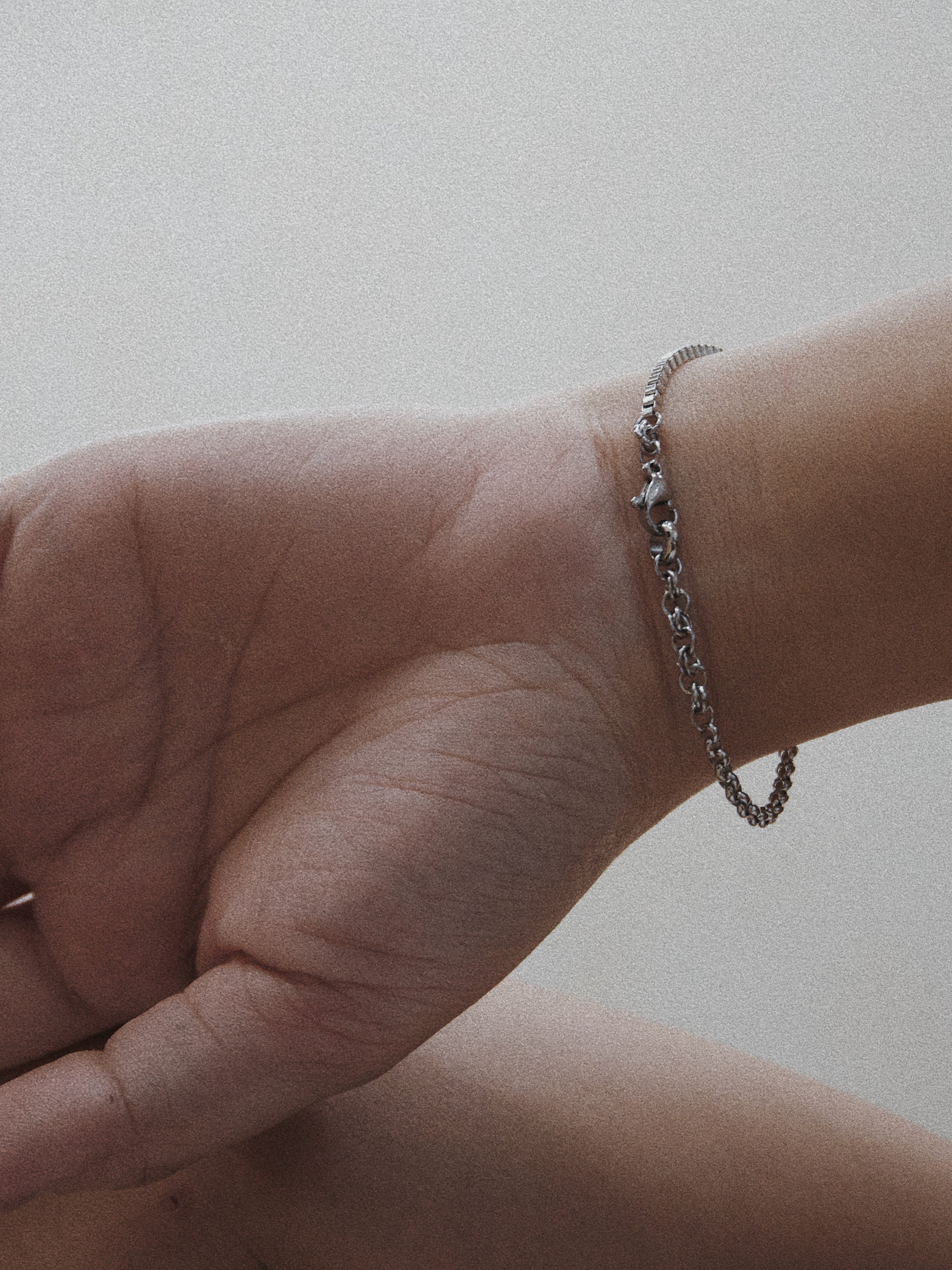 Hand wearing a silver chain bracelet on a plain background