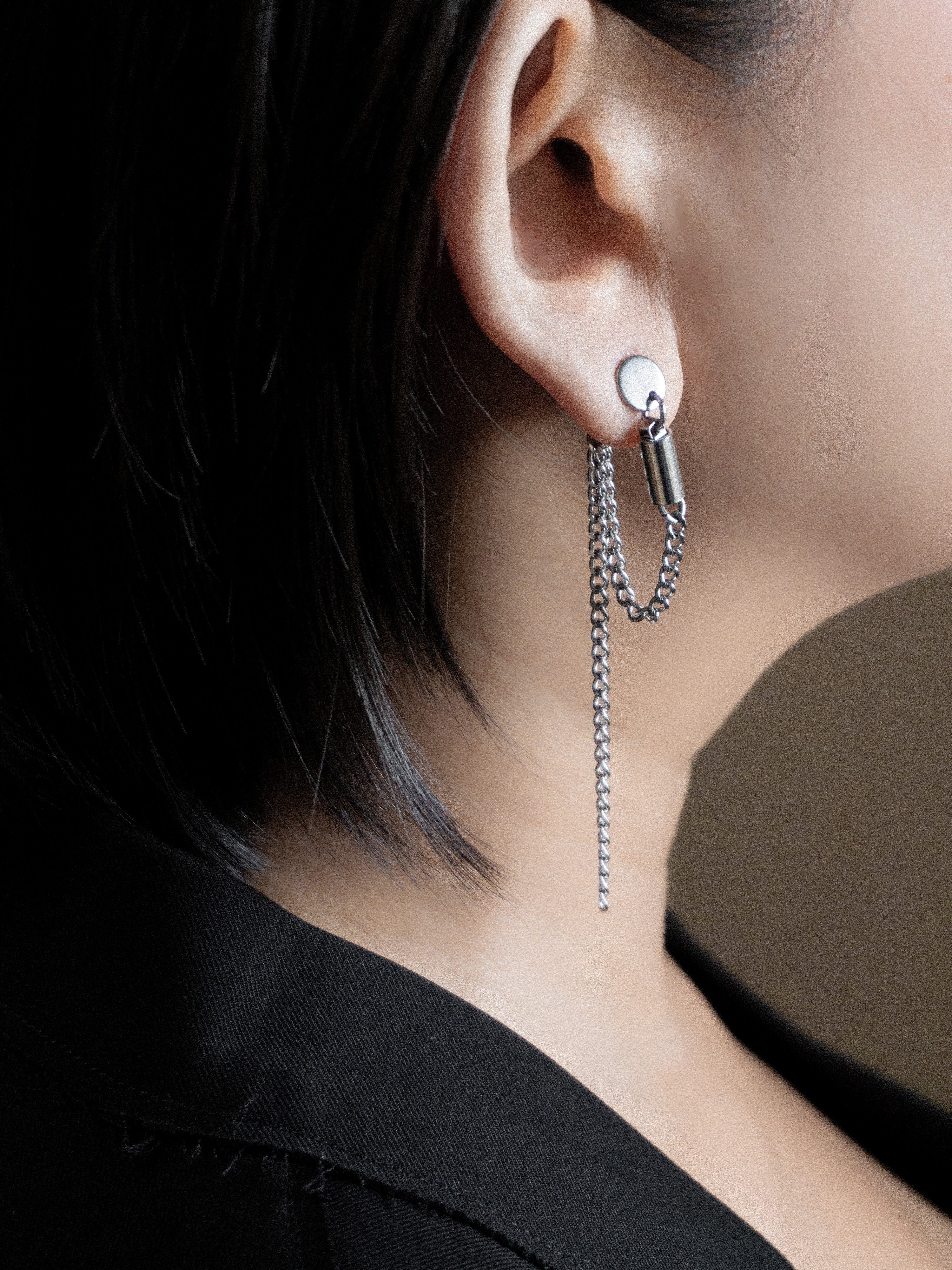 Close-up of an ear wearing a silver earring with a chain detail.