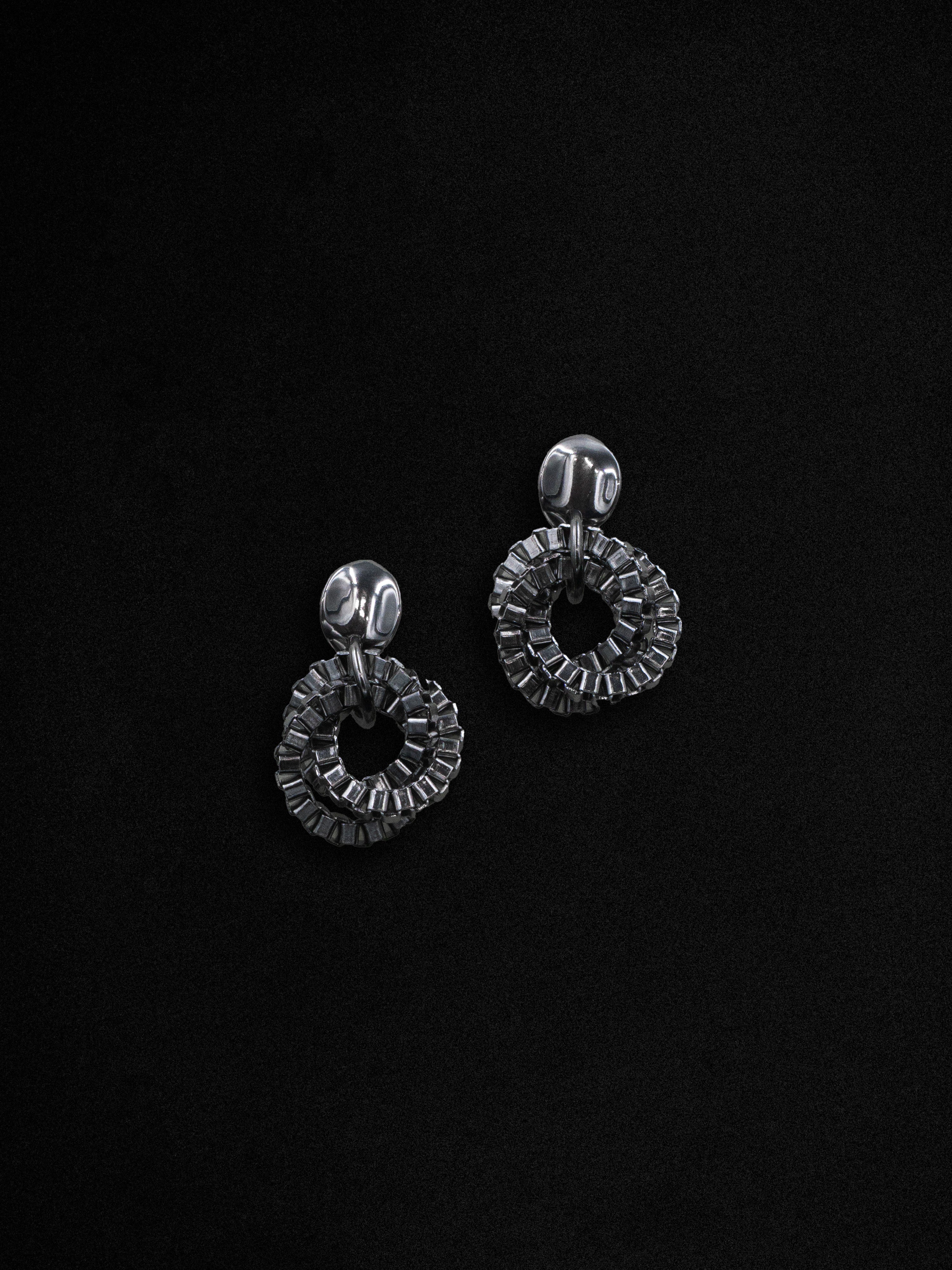 A pair of silver hoop earrings with a swirling design, displayed against a black background.