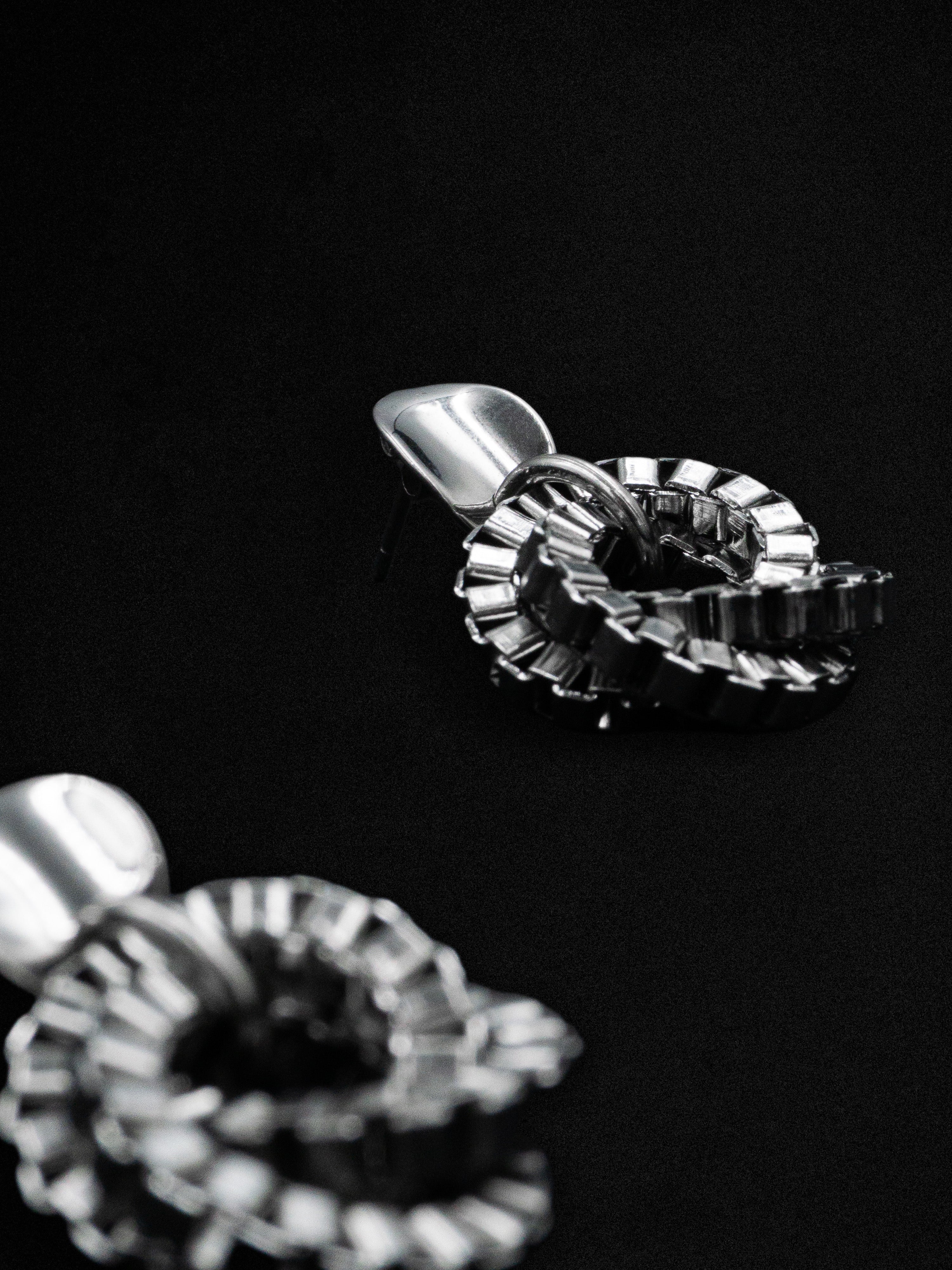 Close-up of silver earrings with an interlocking chain design on a dark background.