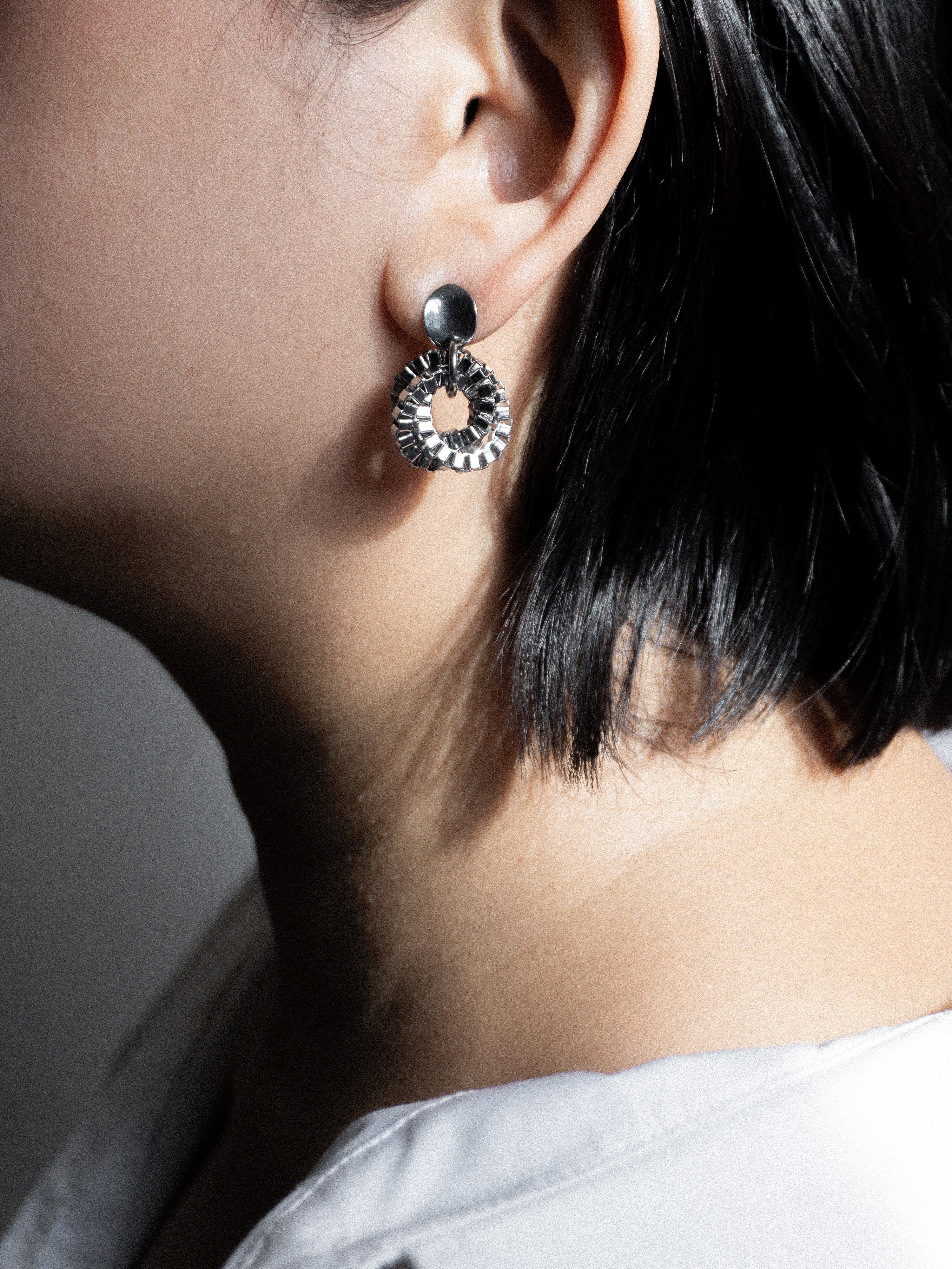 Close-up of a person wearing a silver earring with a circular design.
