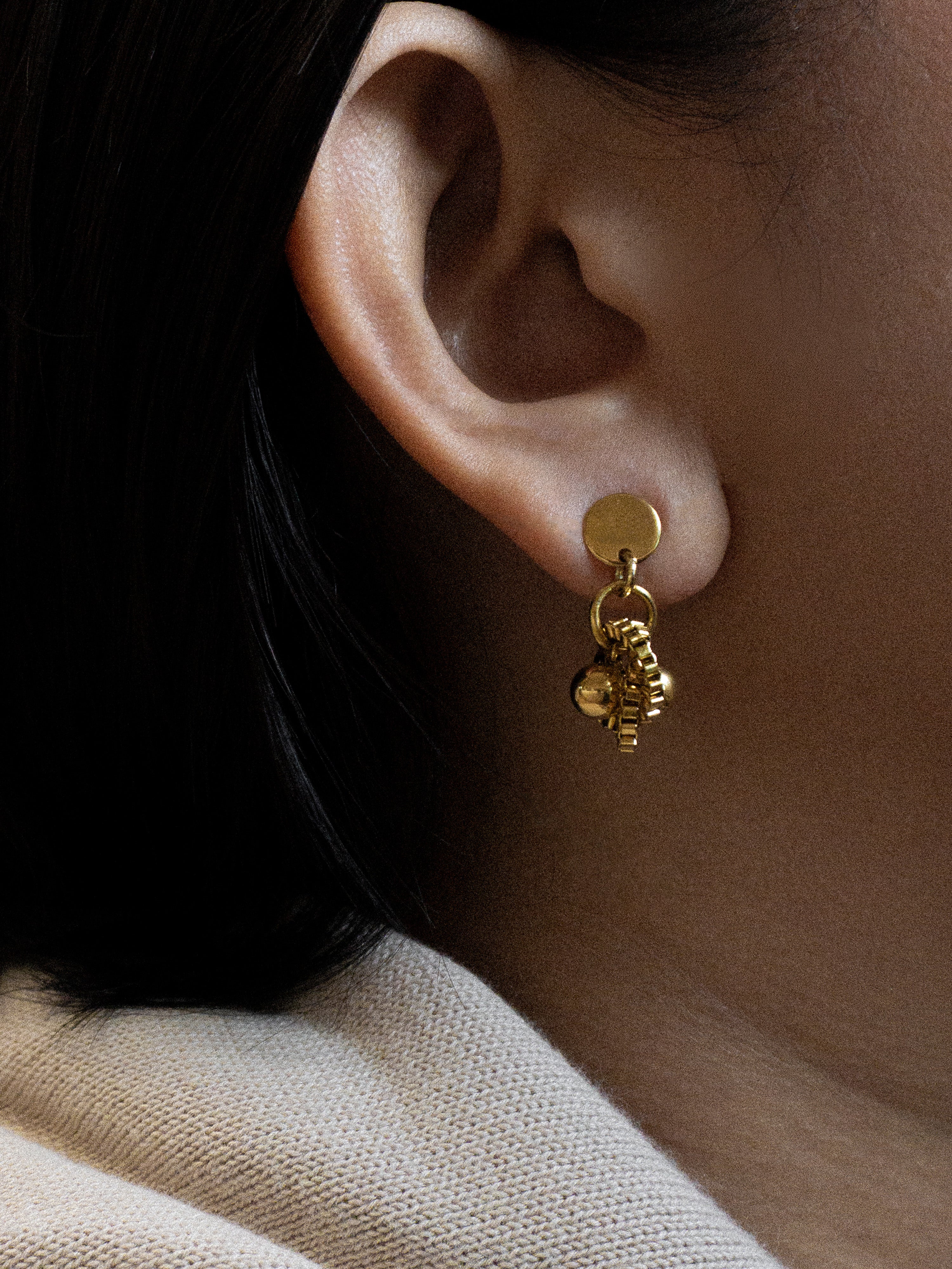 Close-up of an ear wearing a gold earring with small charms.