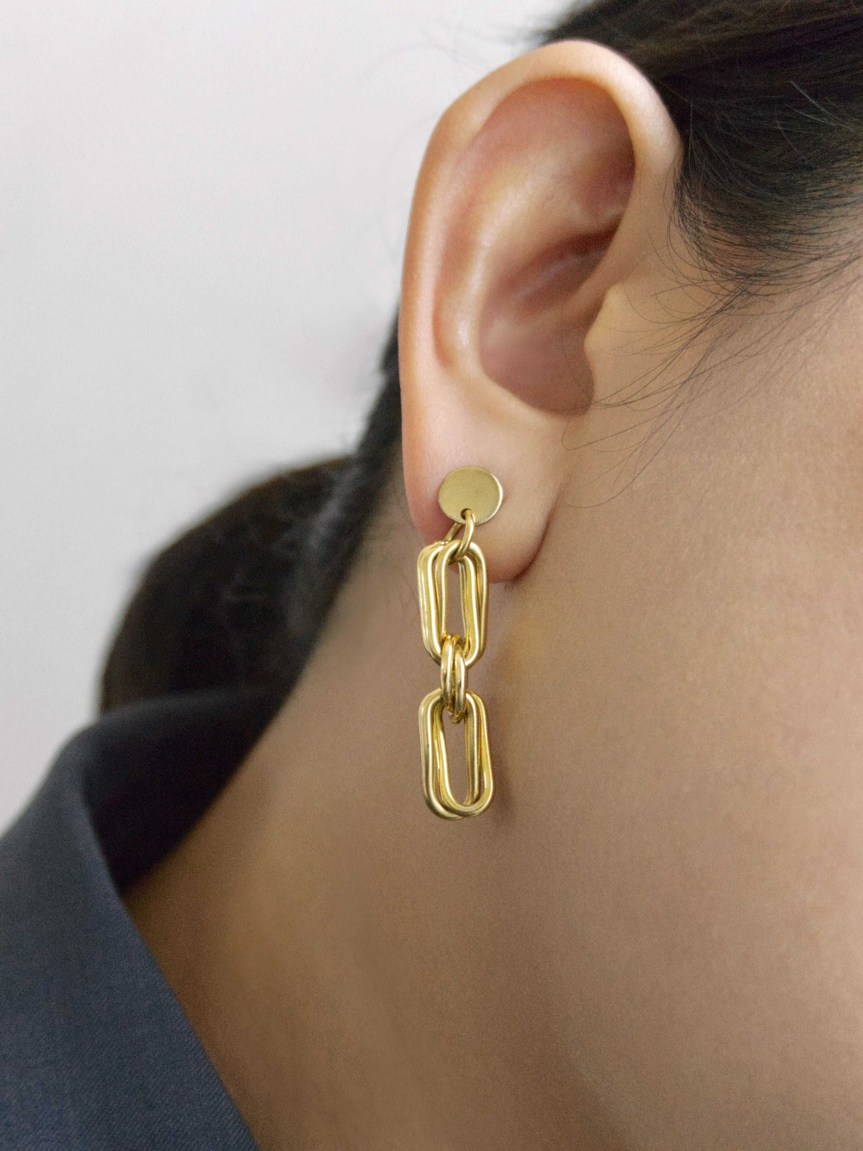 A close-up of a person's ear wearing a gold chain-link dangle earring with a flat circular stud.
