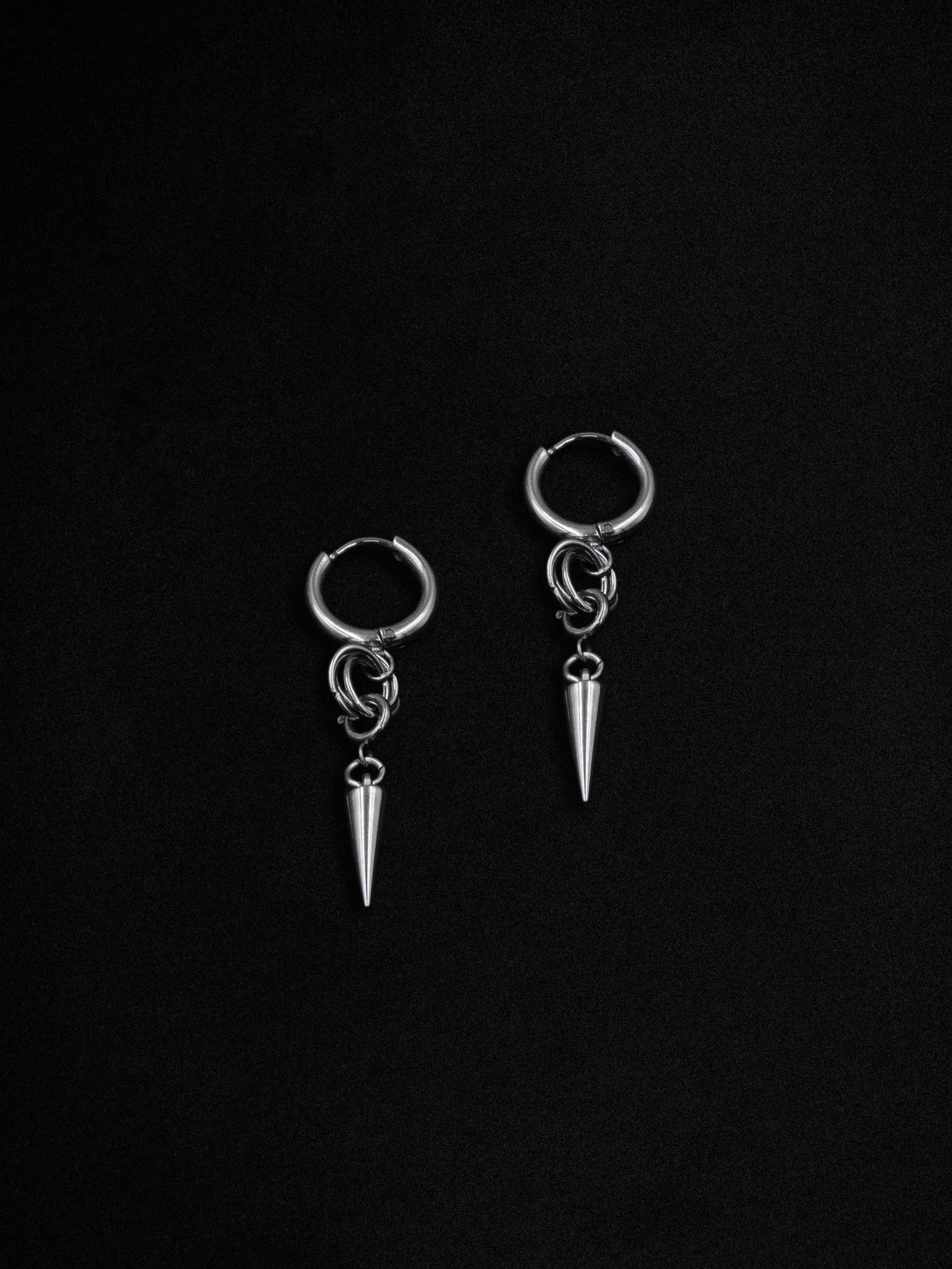 A pair of silver hoop earrings with a pine cone accent and a spike detail, set against a black background.