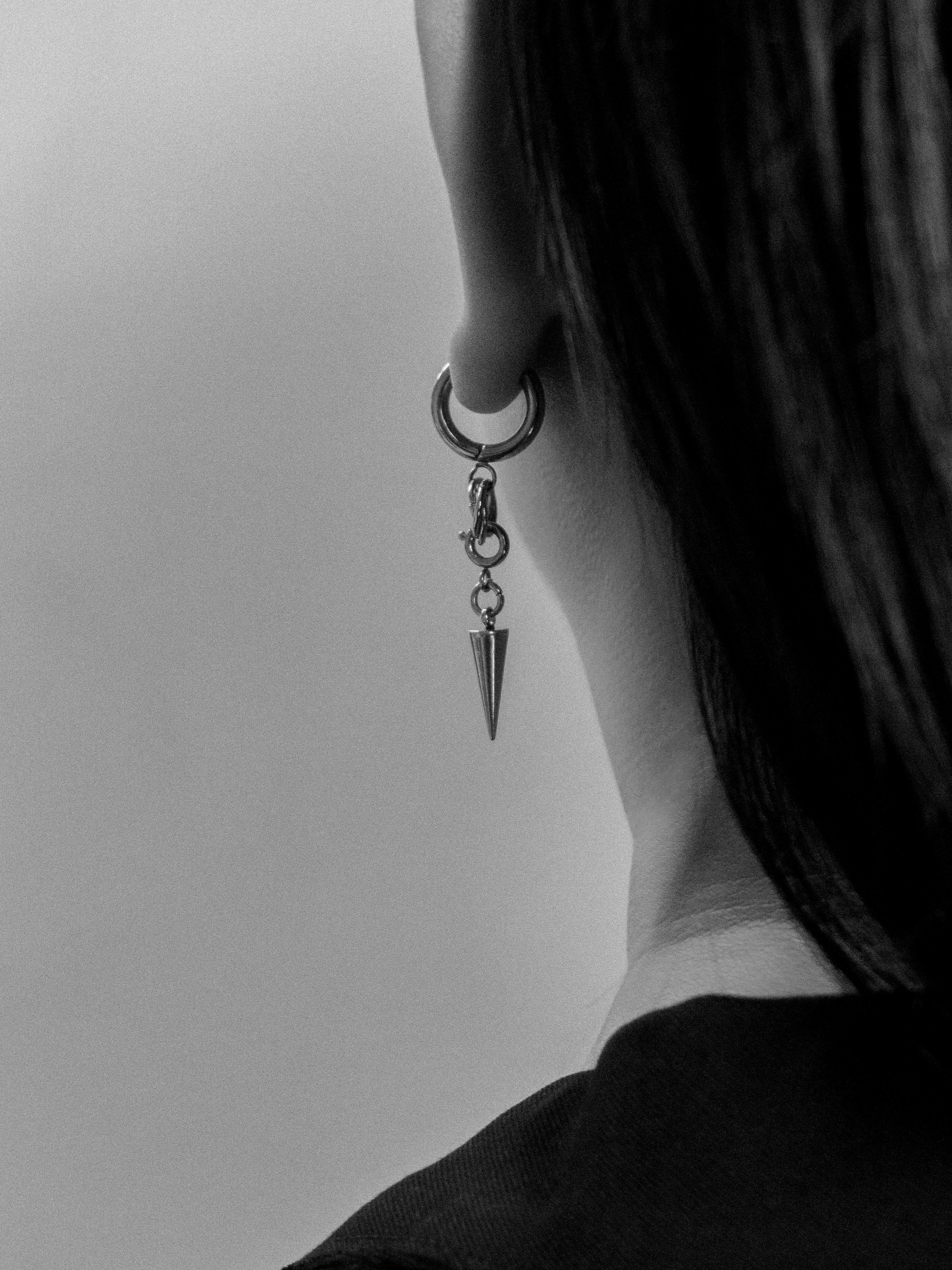 Close-up of a person wearing a dangling earring with a spike on a plain background