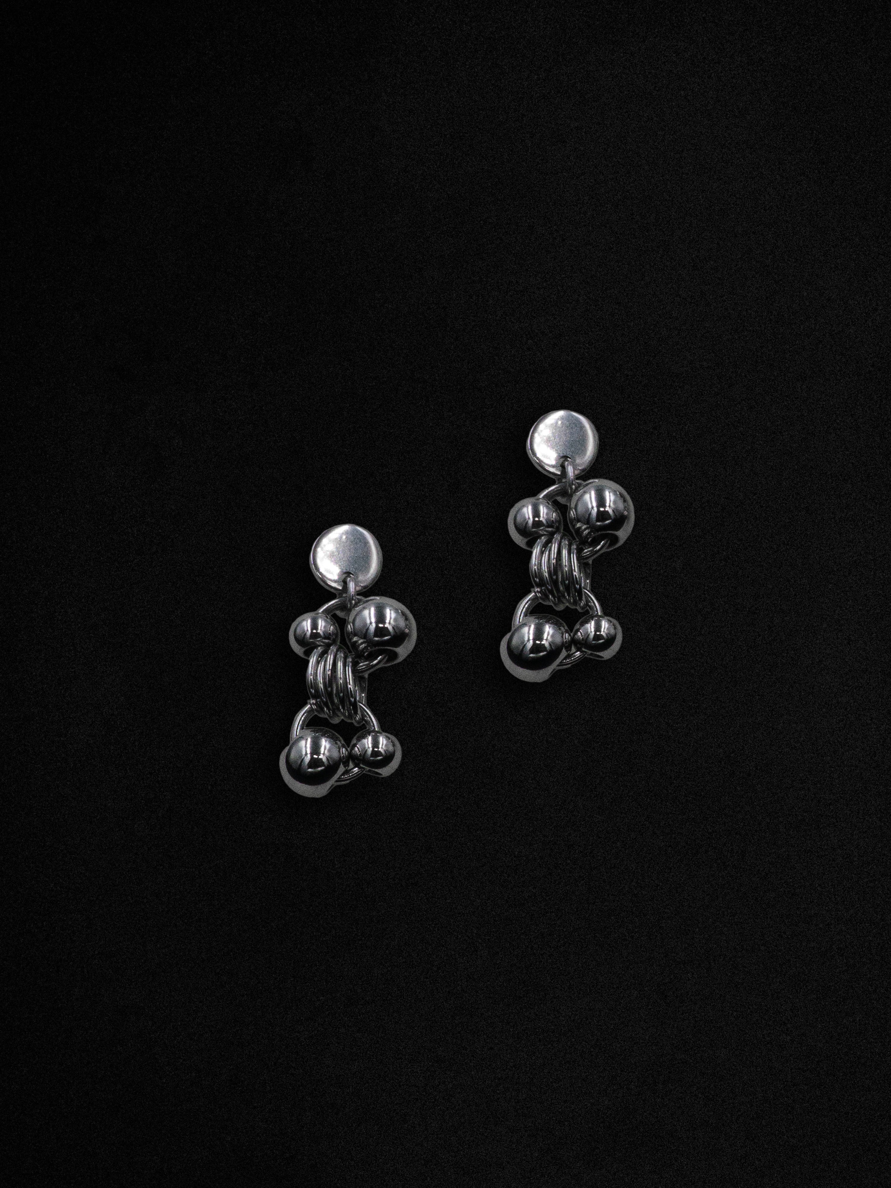 A pair of silver earrings with a geometric design featuring contrasting spheres linked by rings, displayed against a black background.