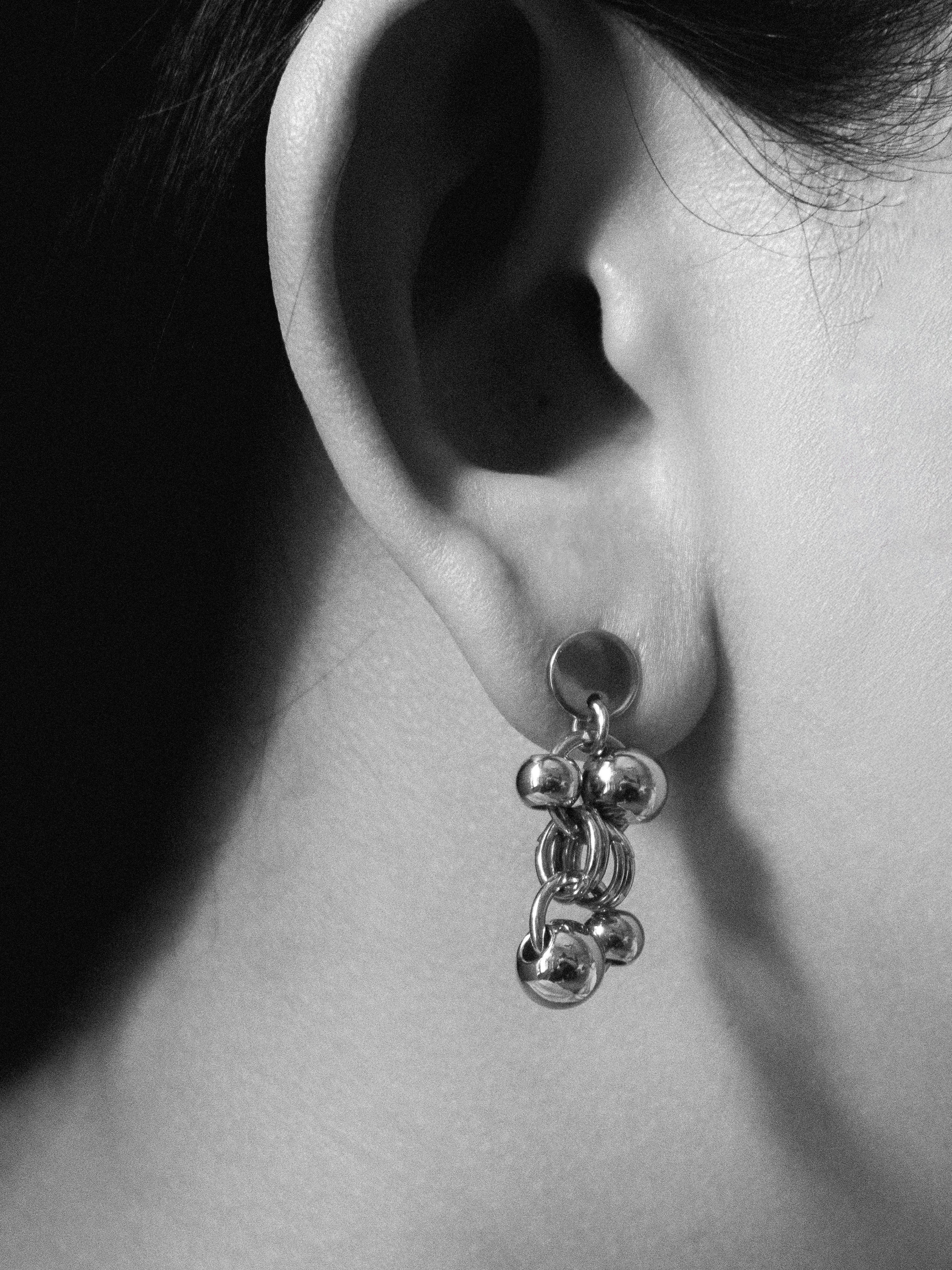 Close-up of an ear wearing a silver earring with dangling beads.