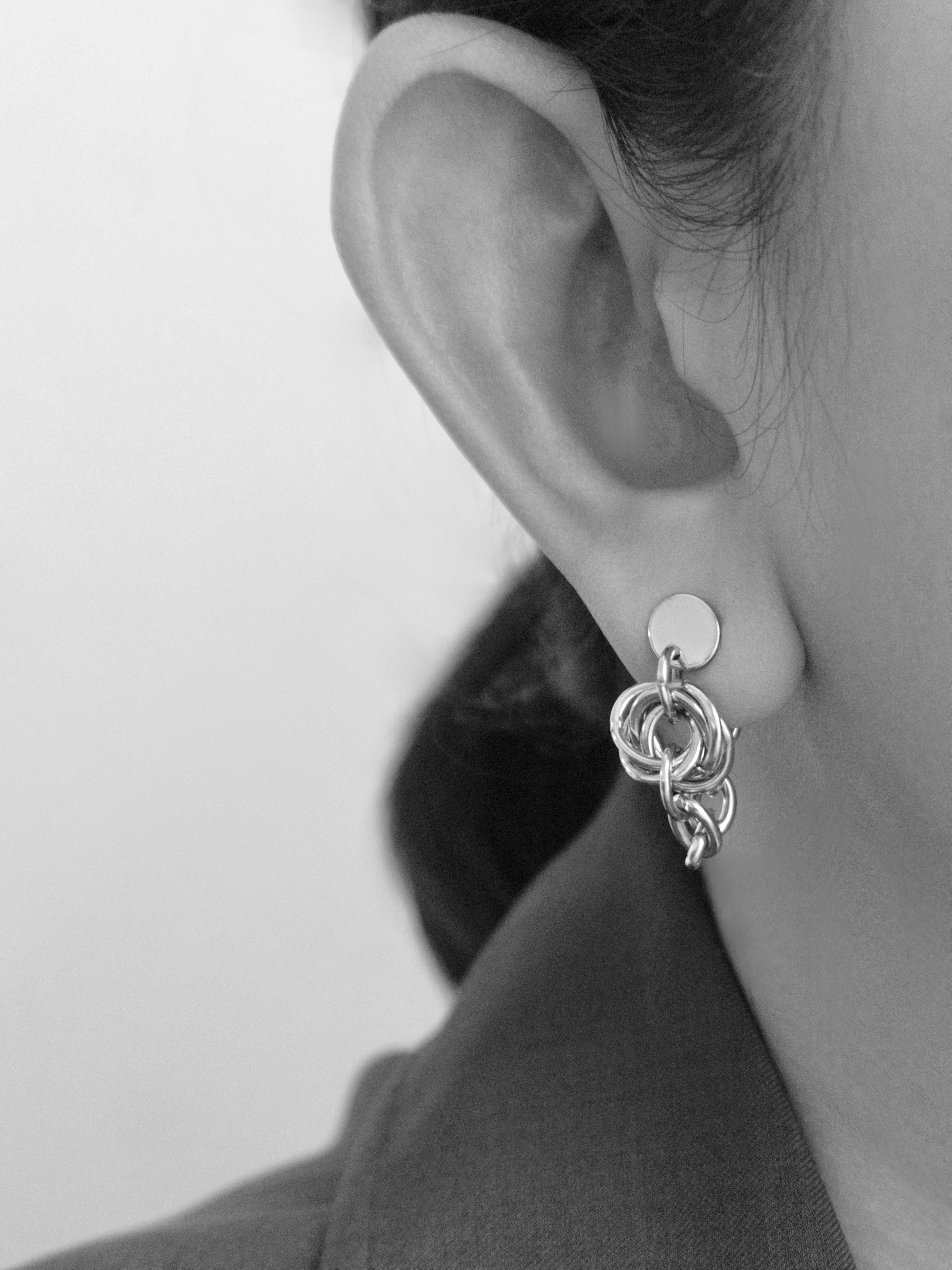 A close-up black and white photo of a person's ear wearing a silver-toned multi-ring hoop earring.