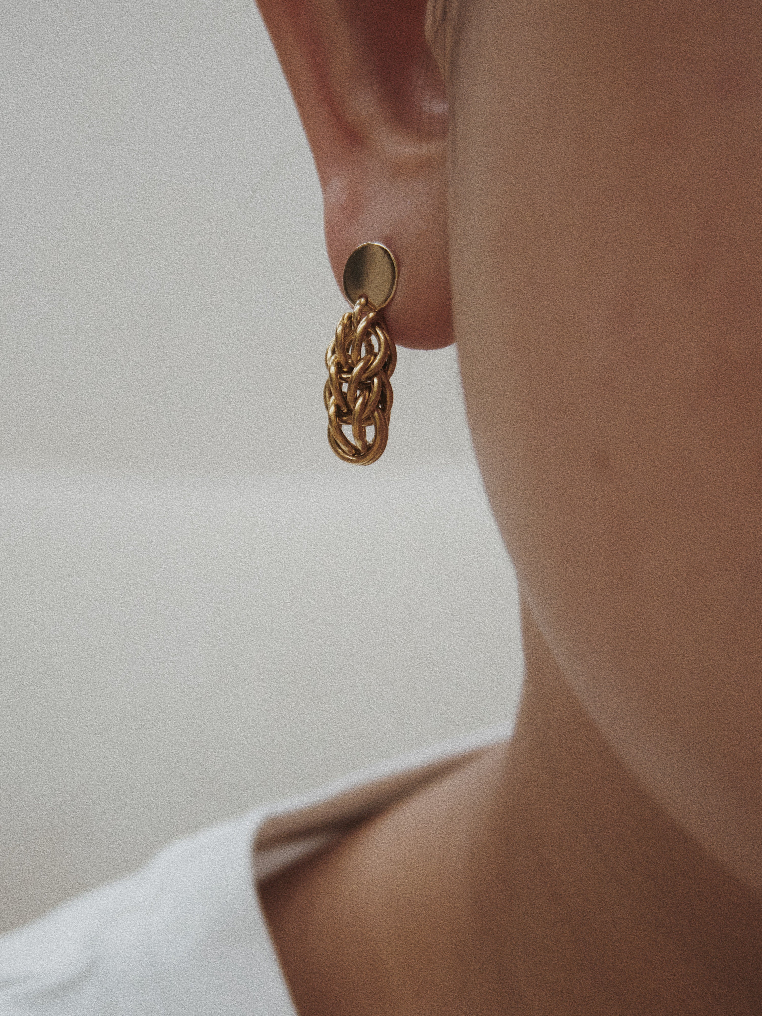 Gold chain earring worn by a person on a neutral background