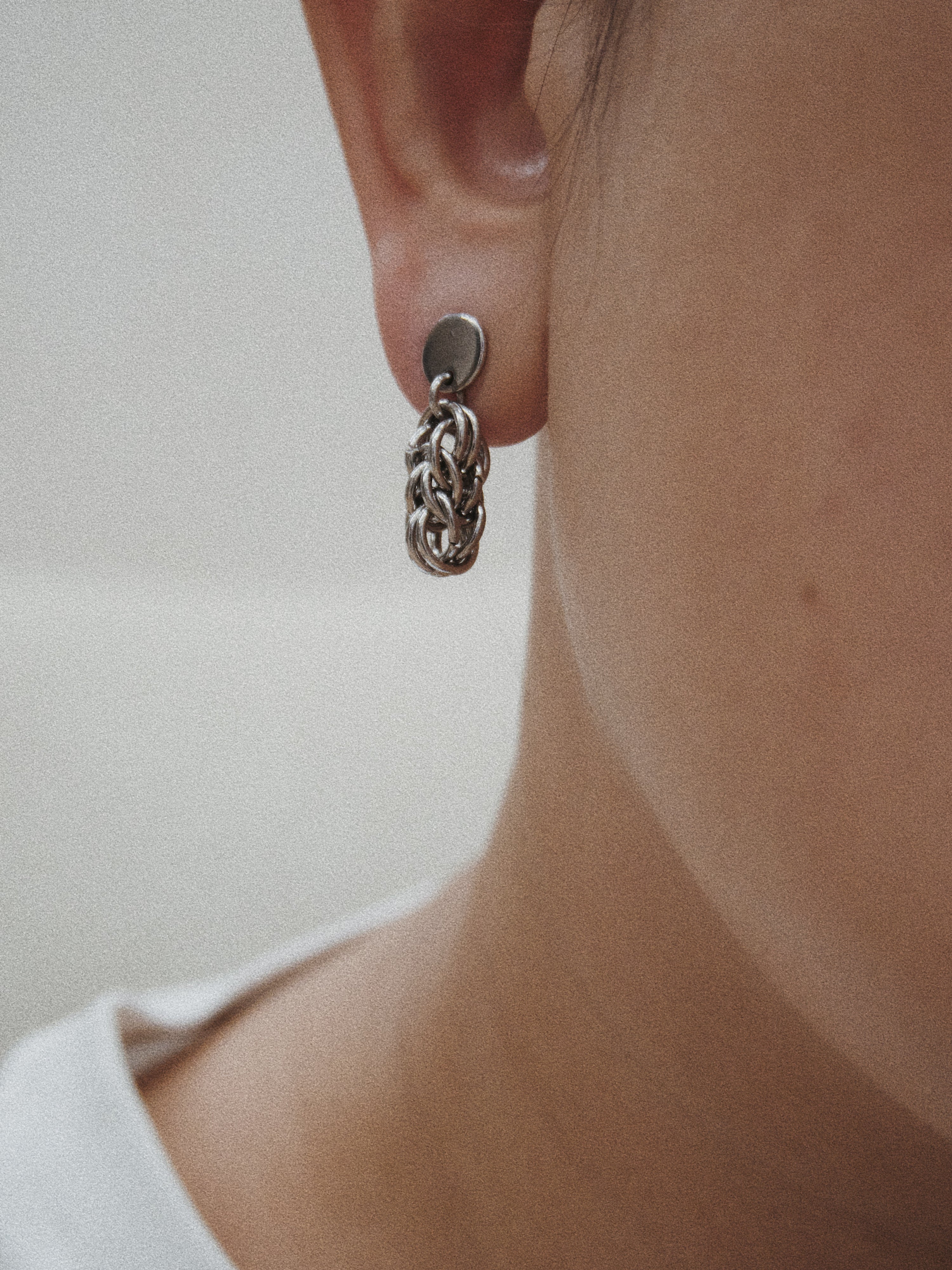 Close-up of a person wearing a silver chain earring against a neutral background