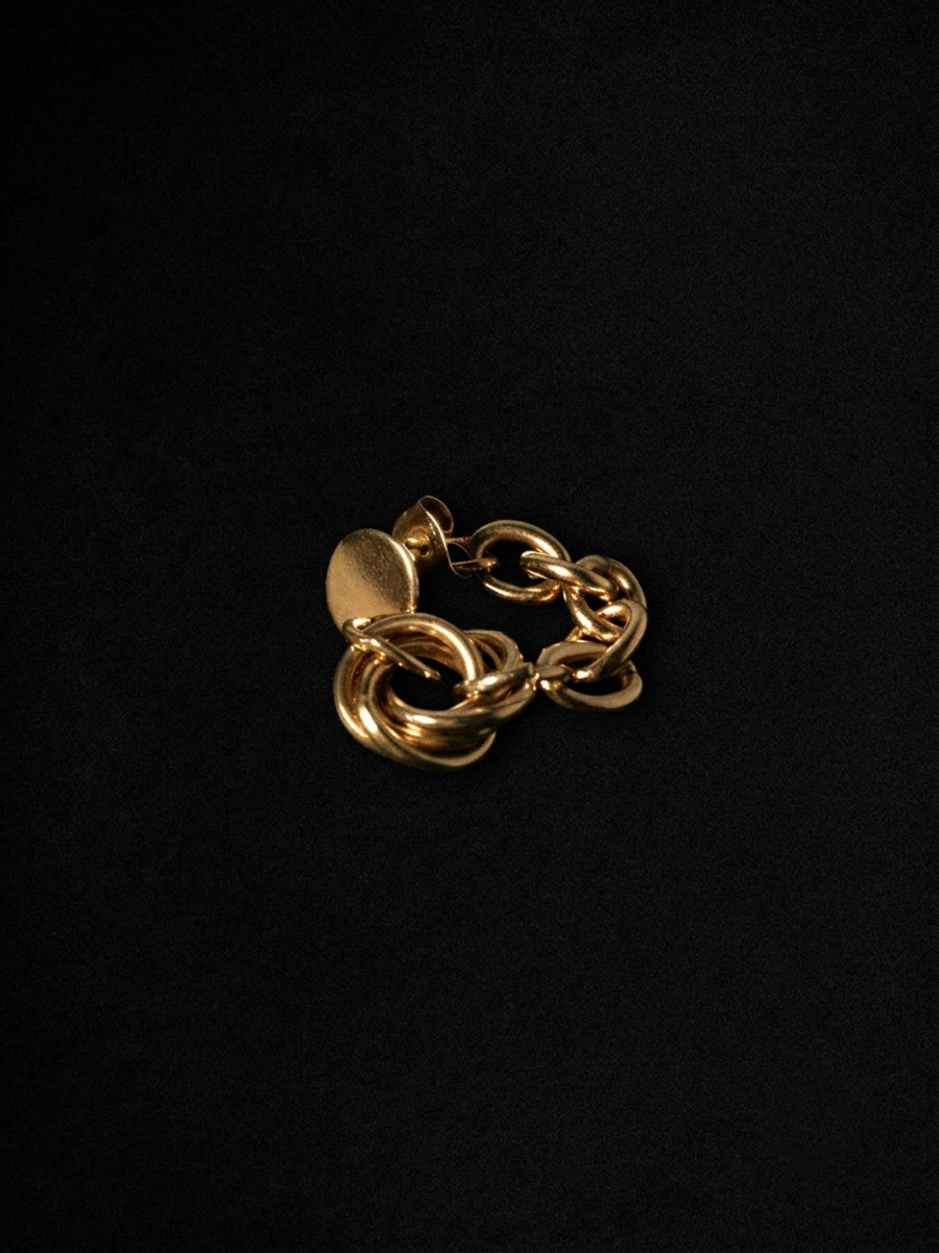 A gold-toned chunky chain link ring with a flat circular disc detail, photographed on a solid black background.