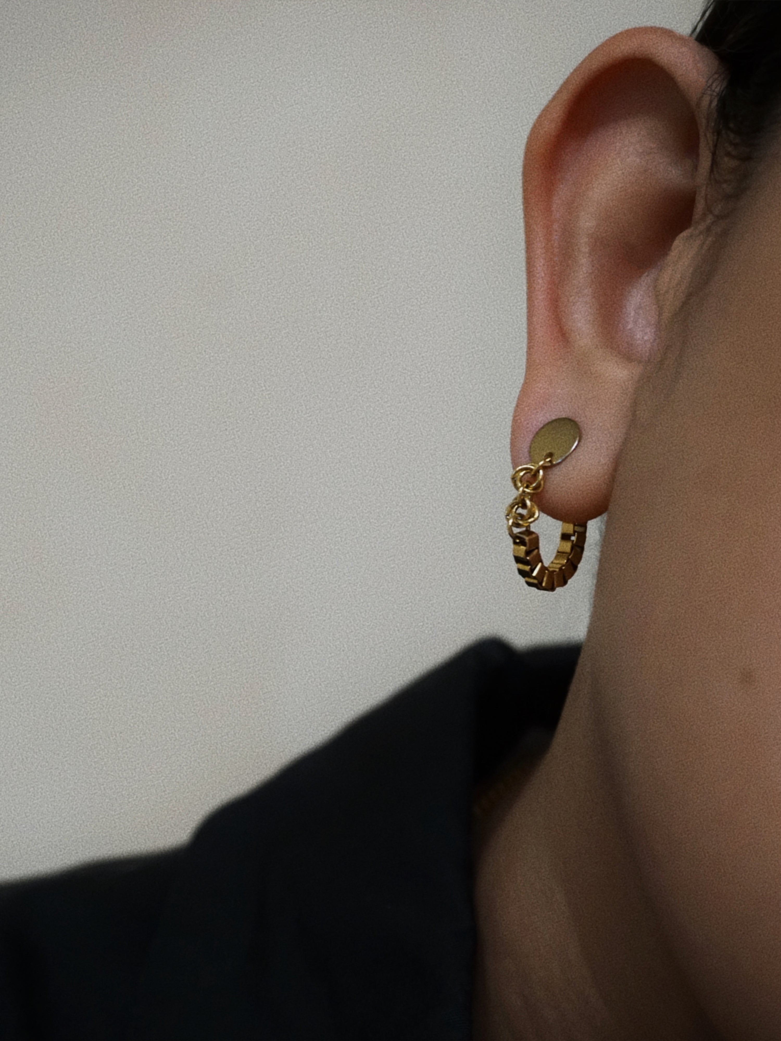 Gold chain earring worn on an ear with a plain background