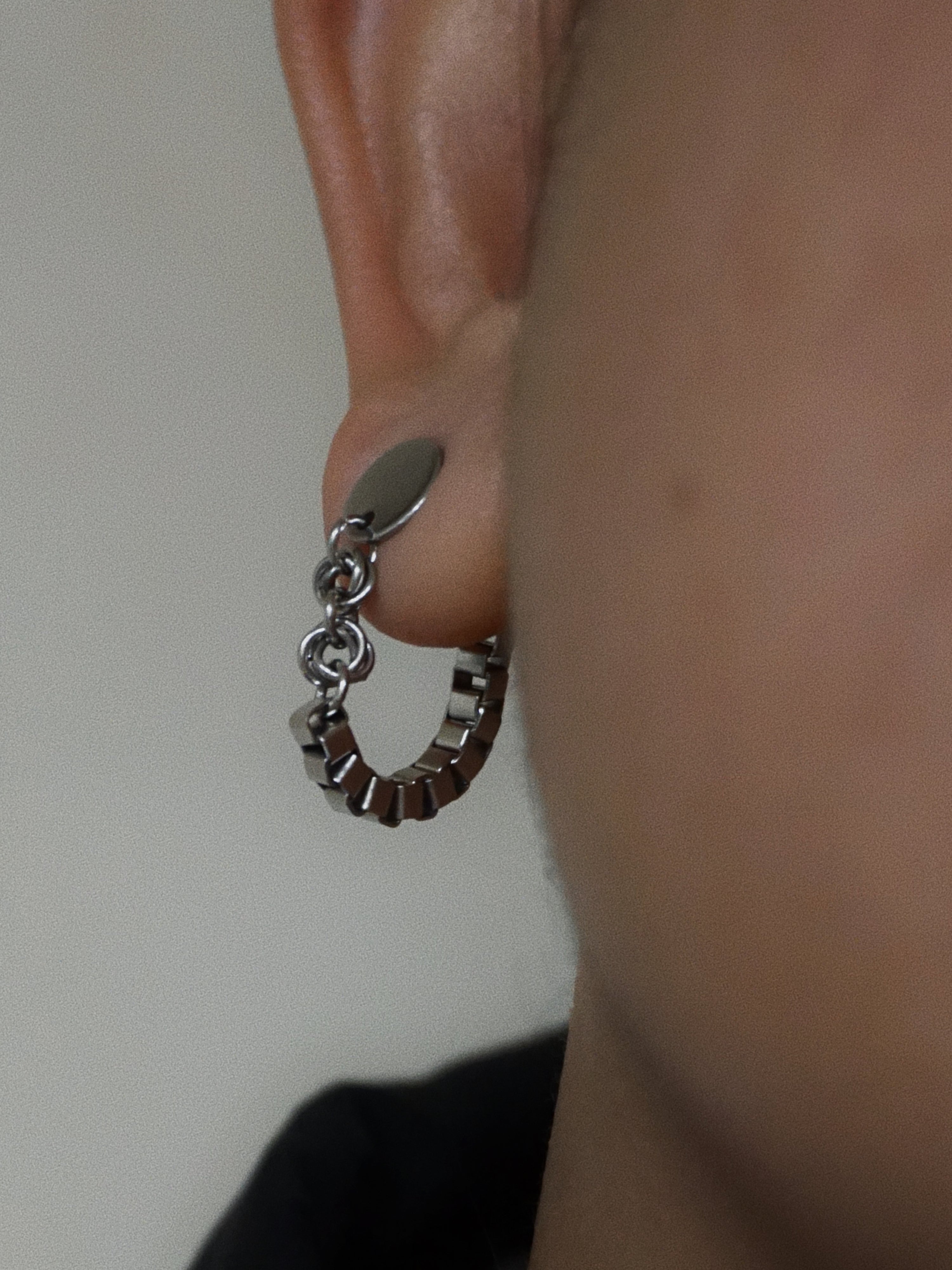 Close-up of a person wearing a silver hoop earring with a chain detail.