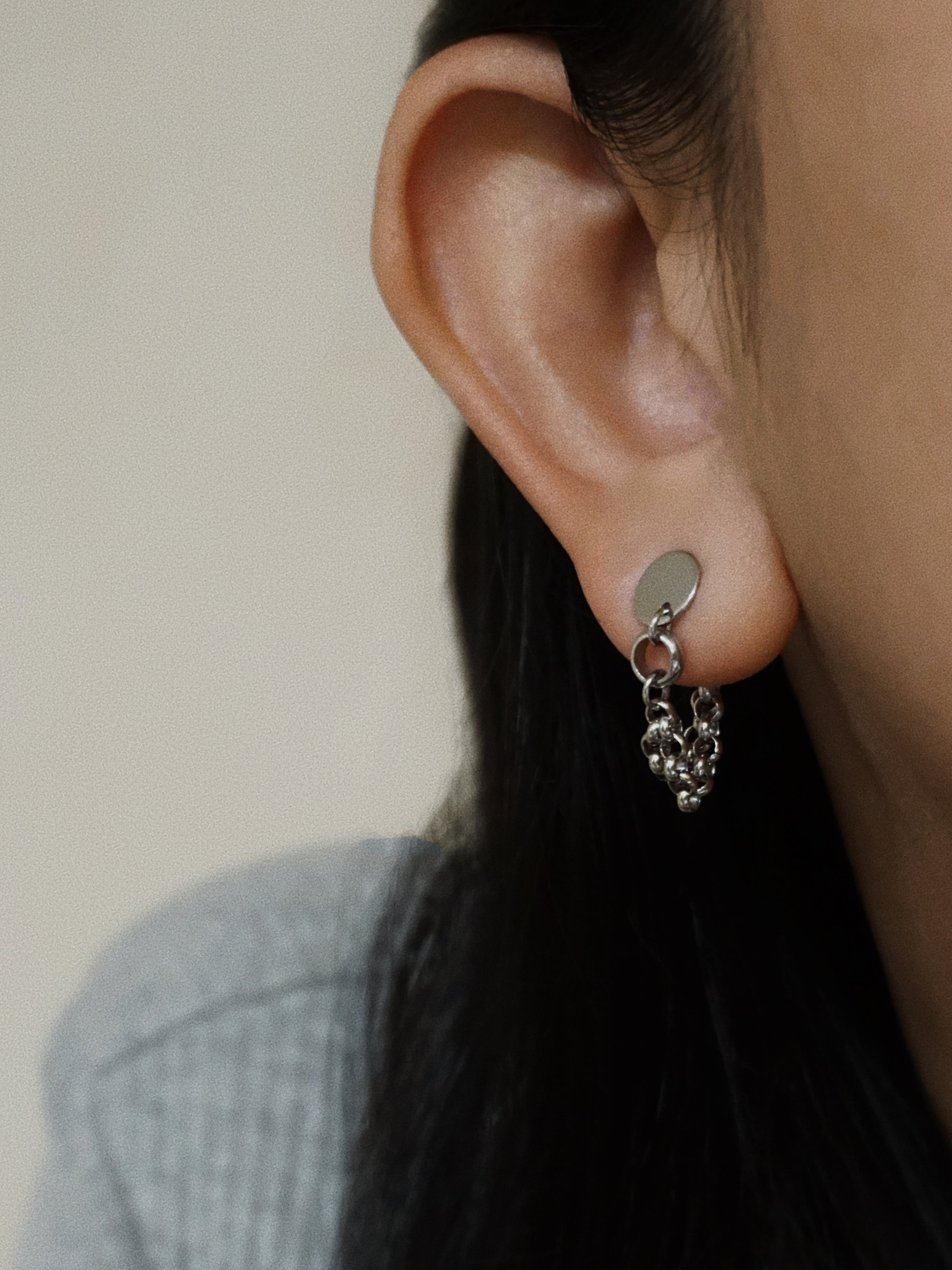 Close-up of an ear wearing a silver earring with a chain detail.