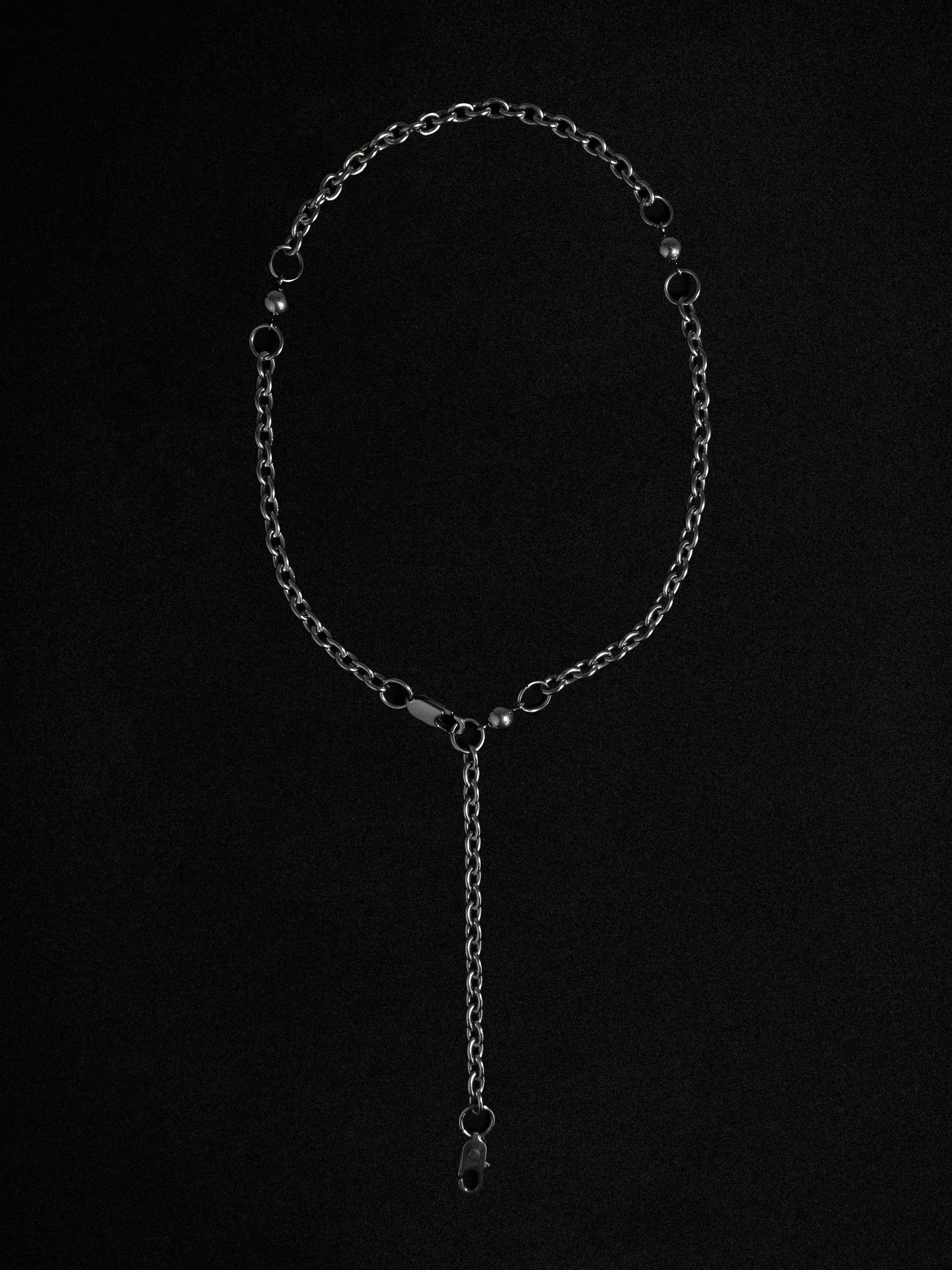 An adjustable necklace with a polished silver-toned steel chain and delicate baubles, presented against a black background.