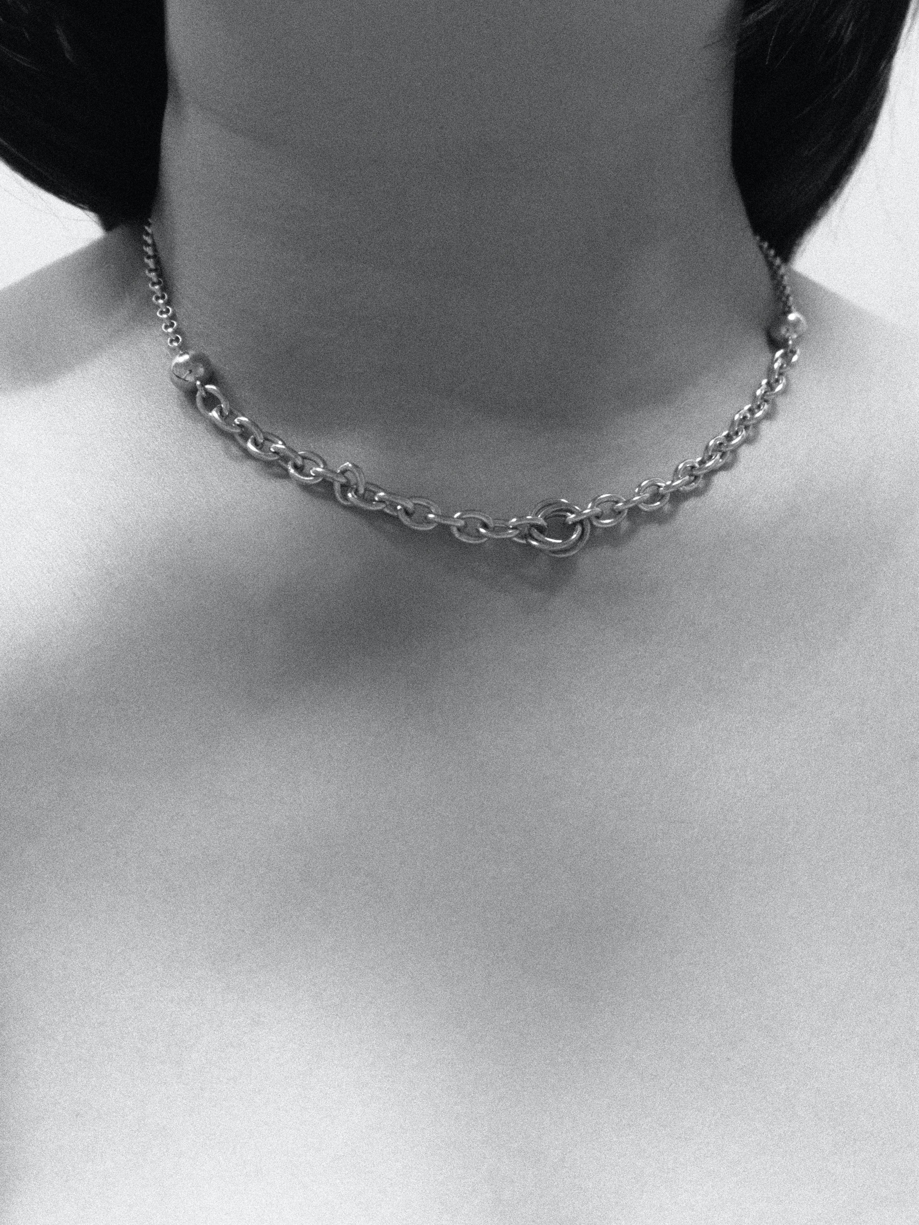 A black and white photograph of a person wearing a silver chain necklace on a plain background