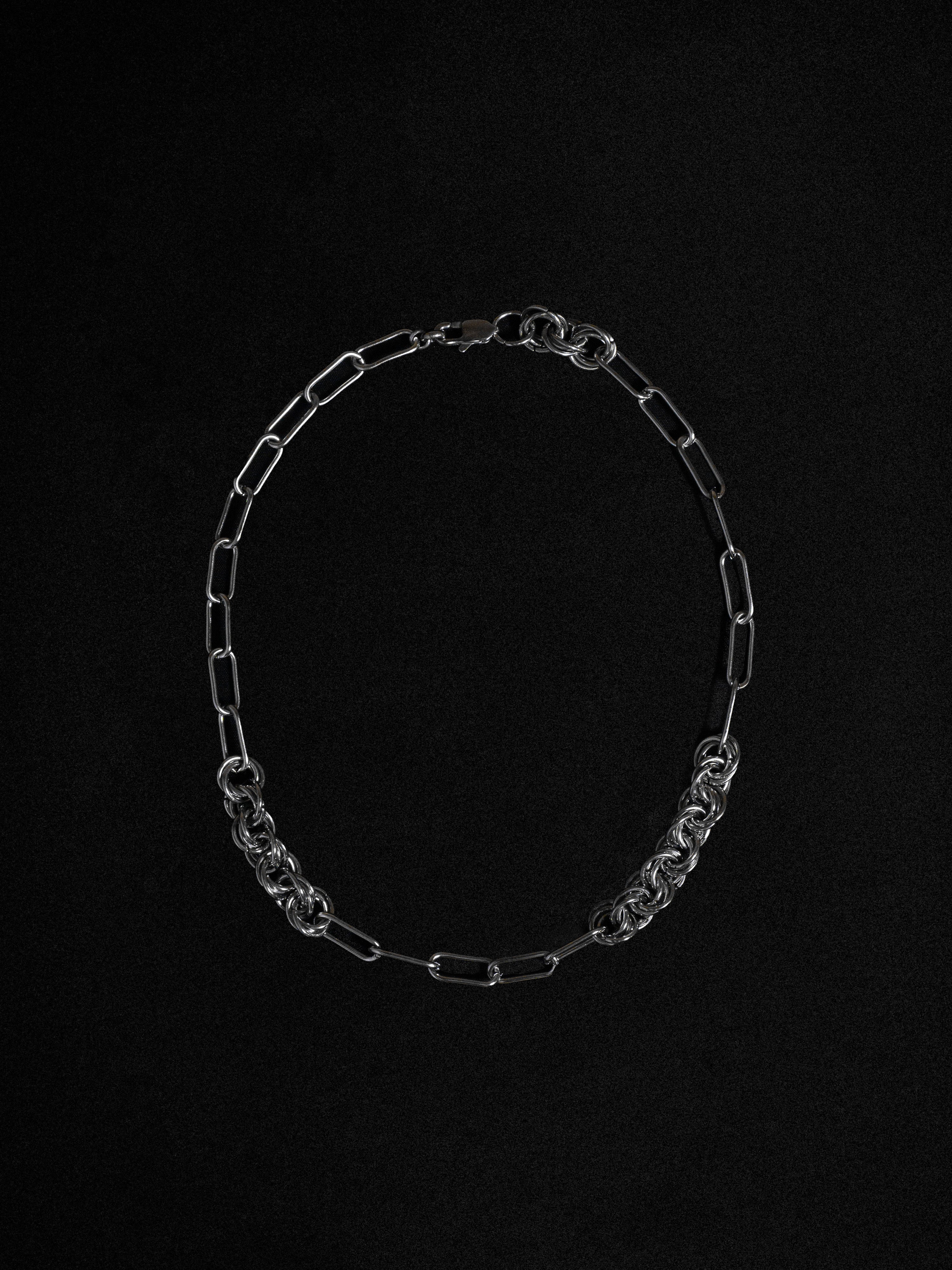 A silver-toned necklace with irregularly interlaced rings, displayed against a black background.