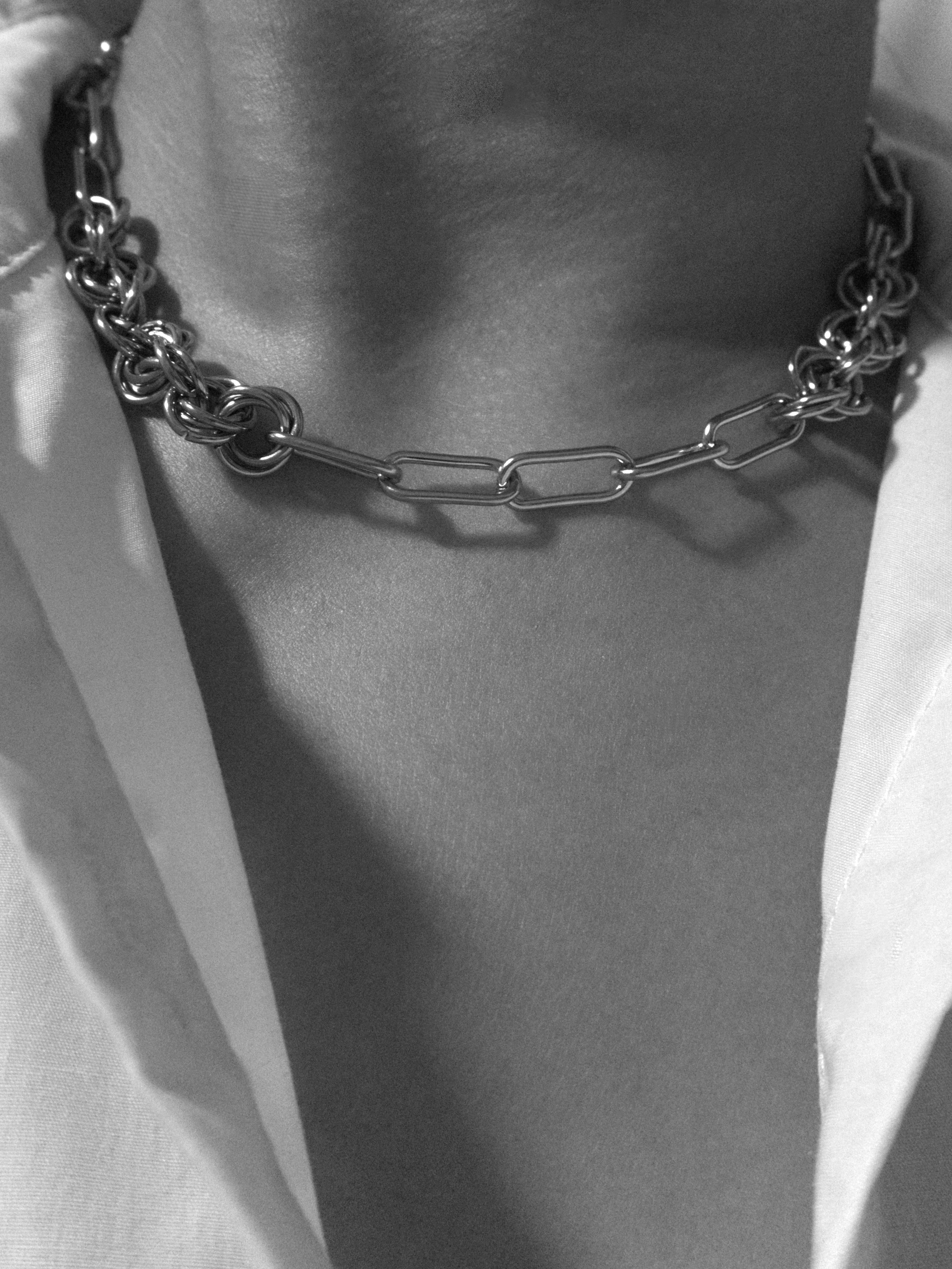 Silver chain necklace on a person's neck wearing a white open collar shirt presented in black and white photograph