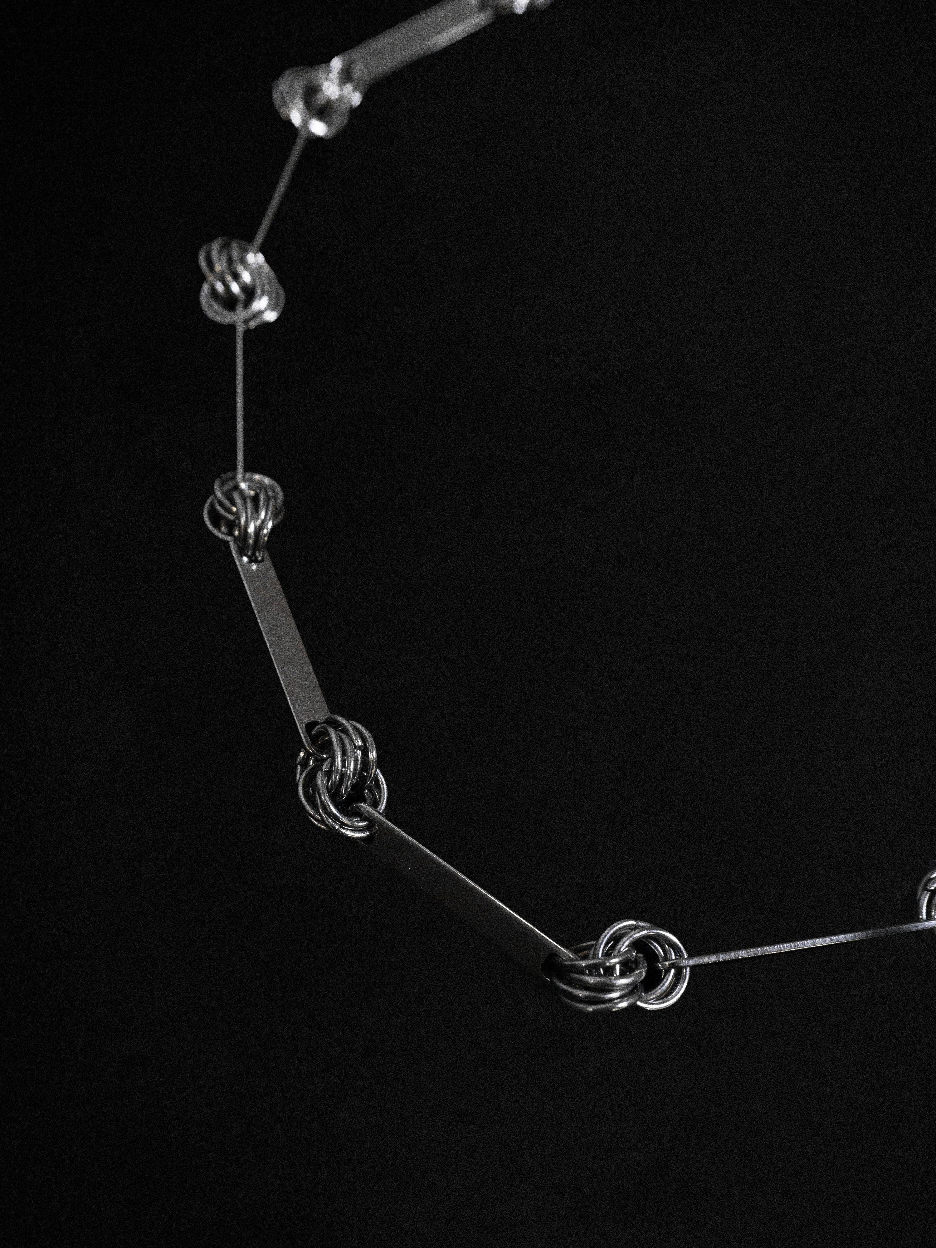 Close up of a silver hardware link necklace with interlinked rings in between against a black background