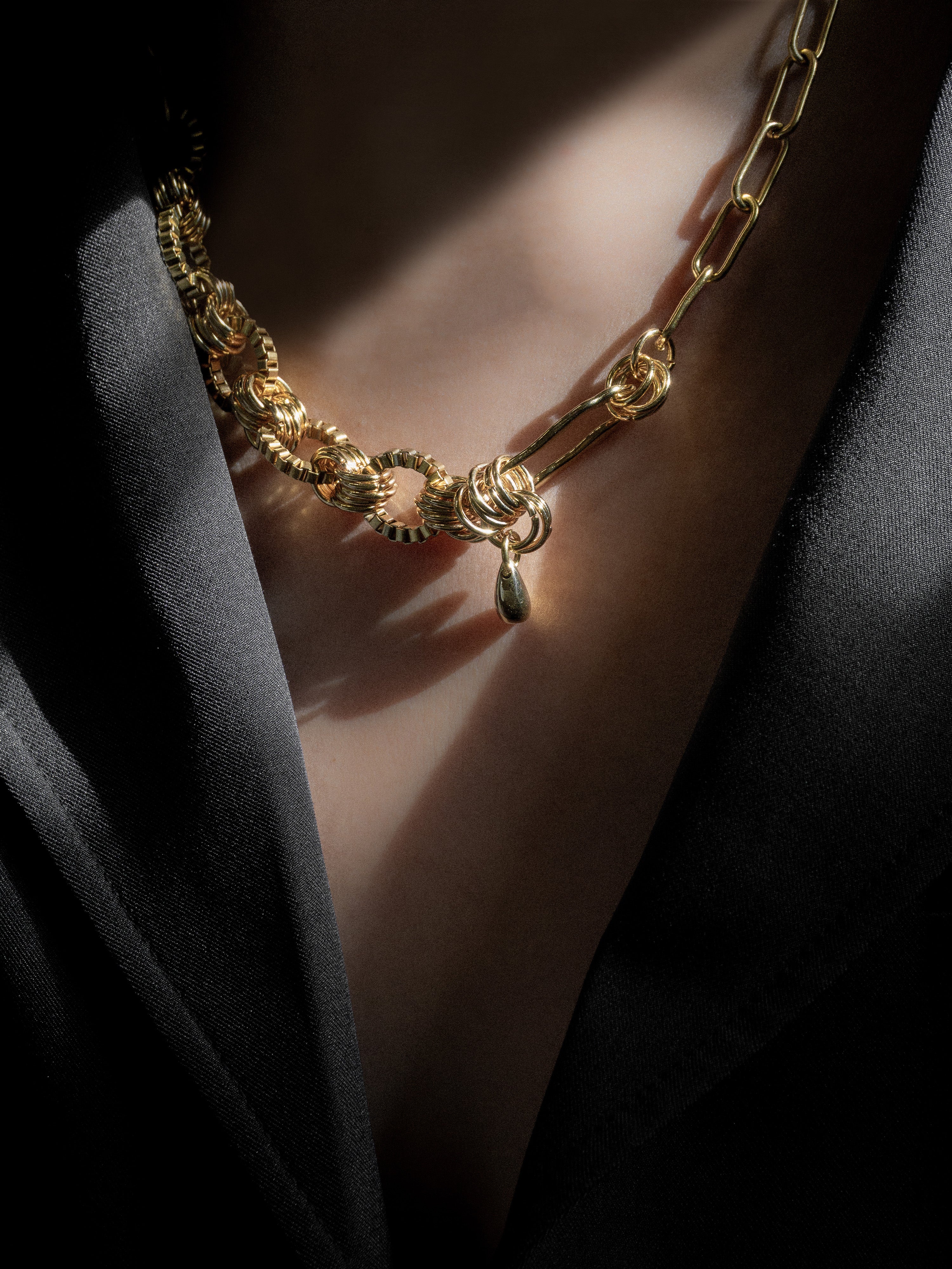 Gold necklace with intricate design on a person wearing black blazer